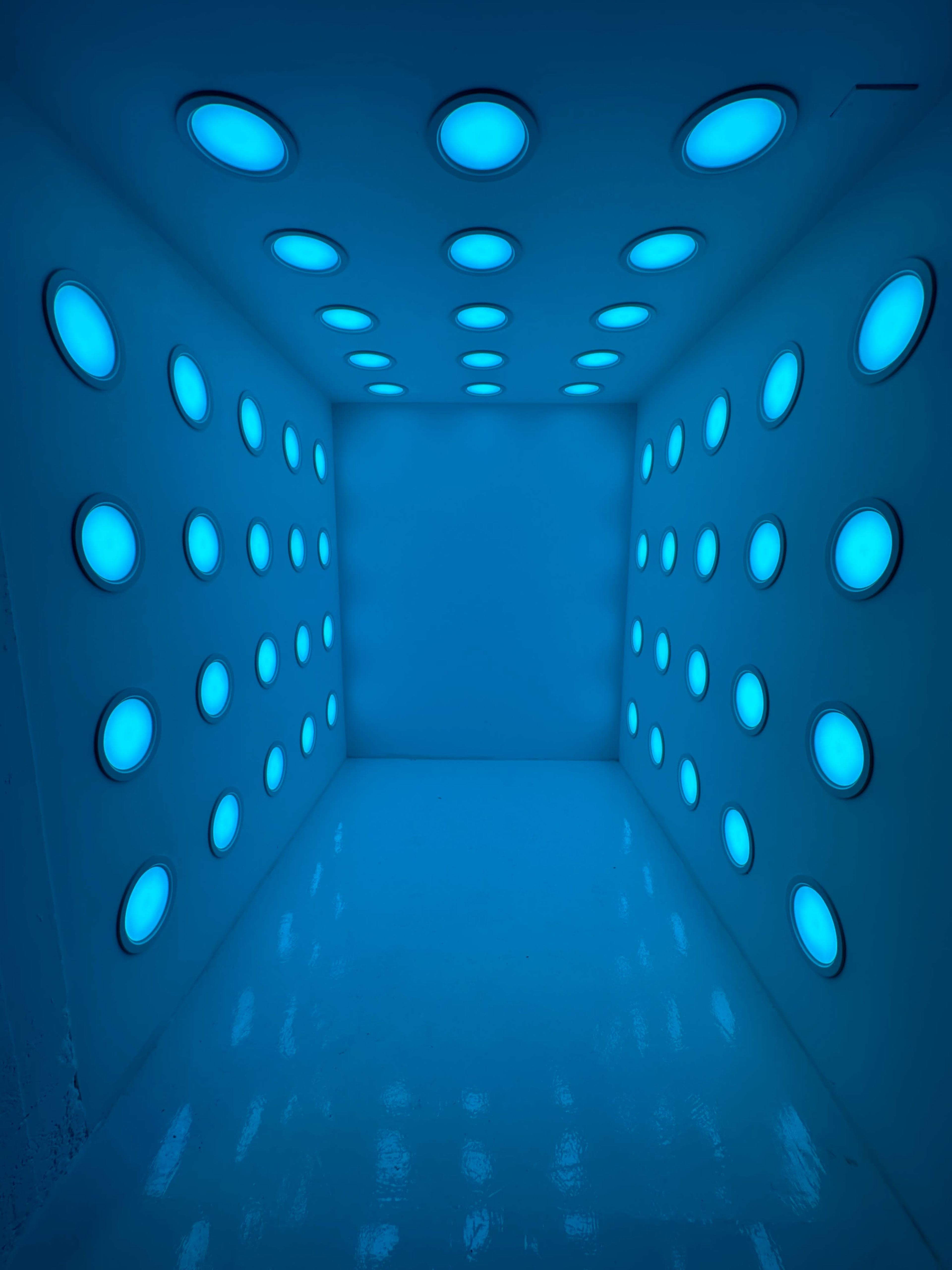 A small, brightly lit room features walls adorned with circular blue lights.