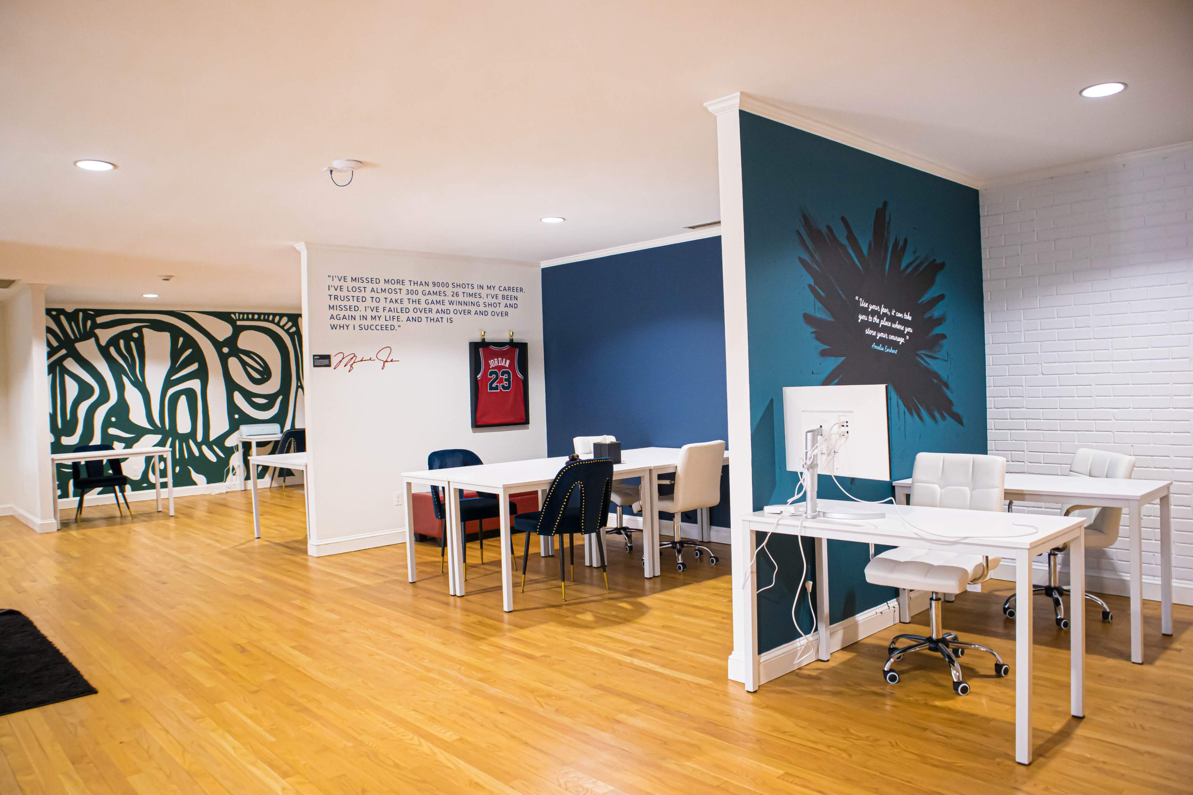 A professional workspace with white desks, chairs, and motivational wall art, featuring a green accent wall and a stylized mural.