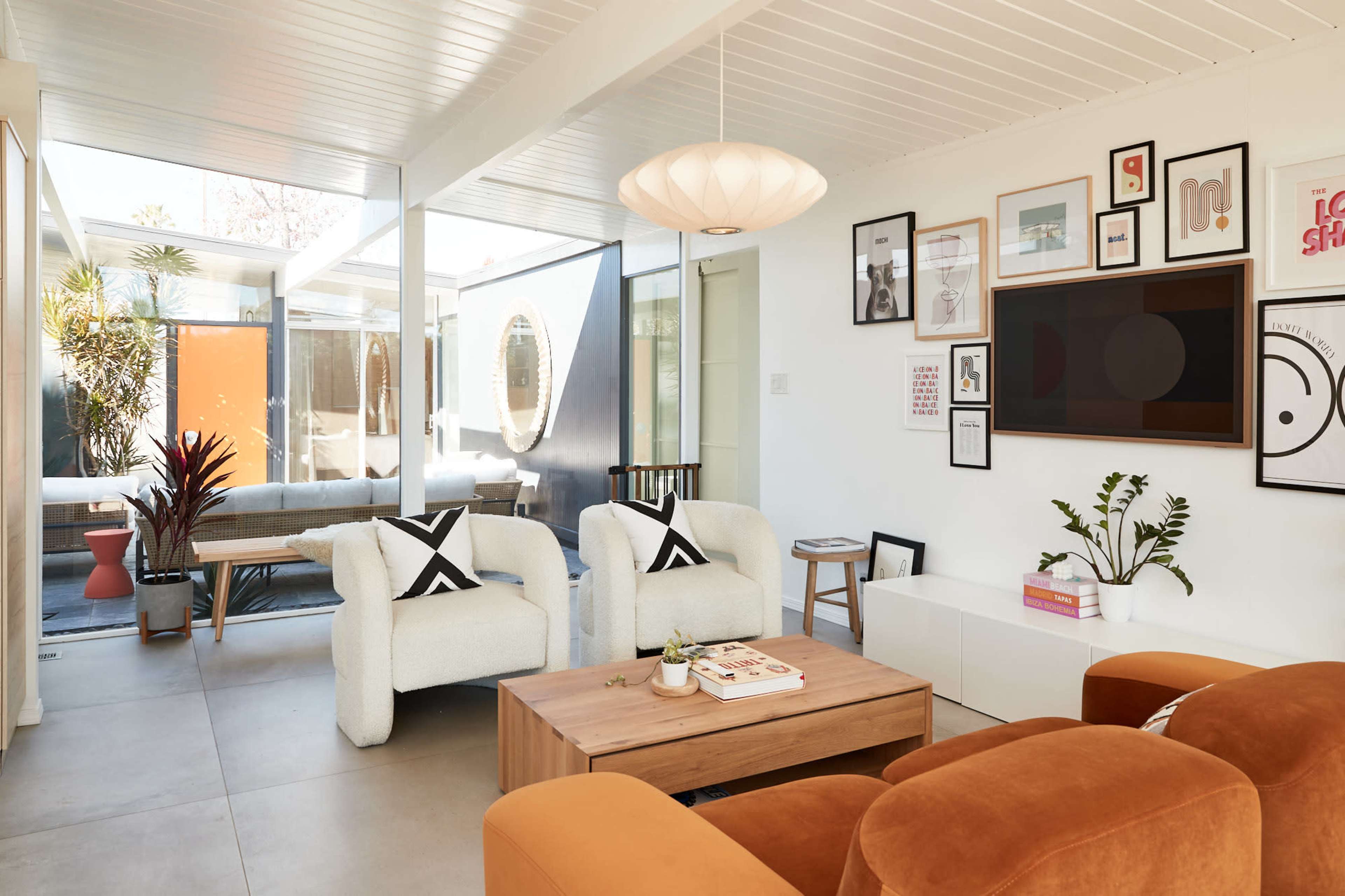A modern living room featuring two armchairs, a coffee table, a large wall-mounted television, and various framed artworks.
