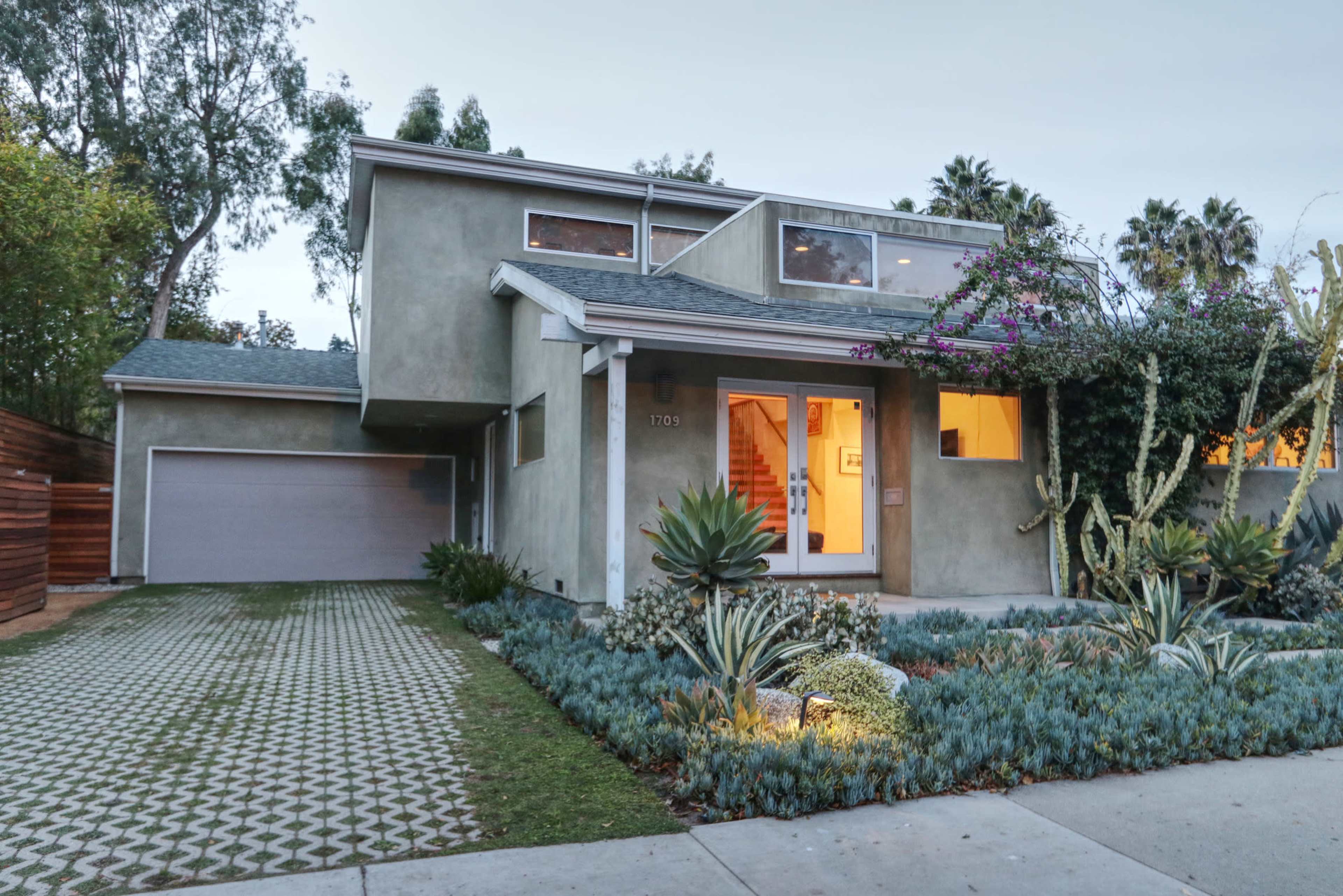 A modern two-story house with a landscaped front yard featuring succulents and a driveway lined with patterned pavers.