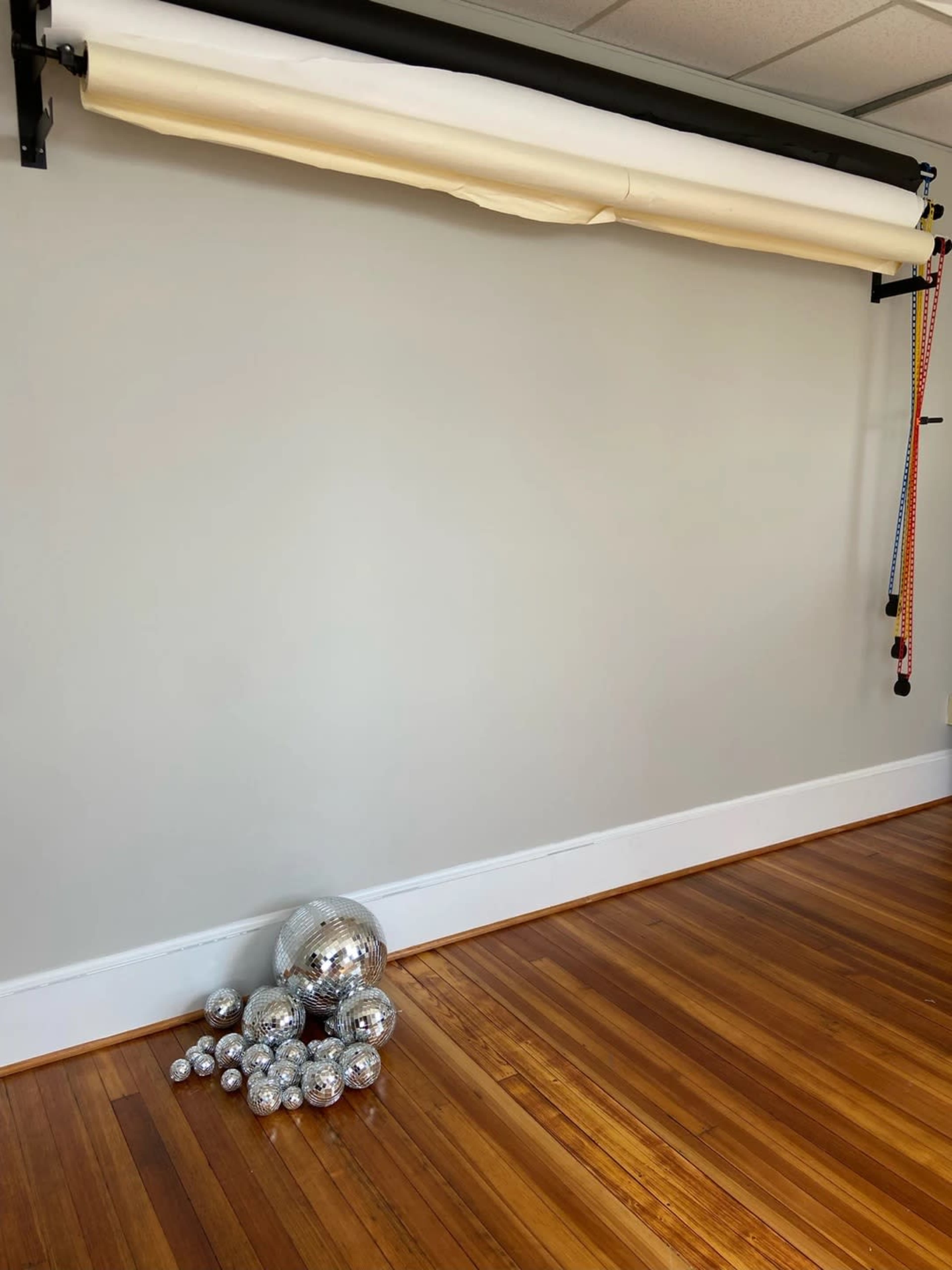 A row of mirrors balls of various sizes is placed on a wooden floor in front of a plain wall with a backdrop support system.