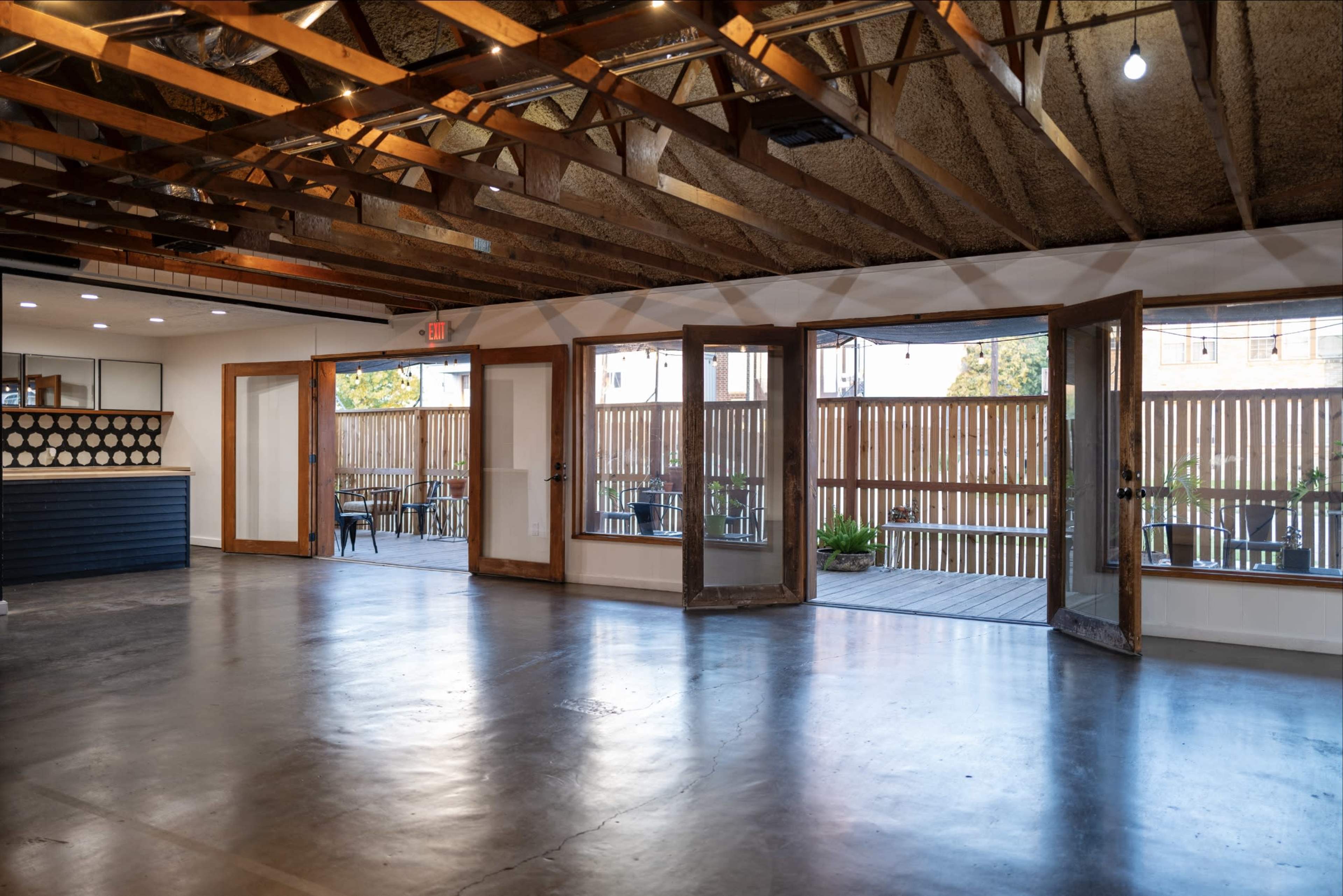An open interior space with wooden beams, concrete flooring, and large double doors leading to an outdoor area.