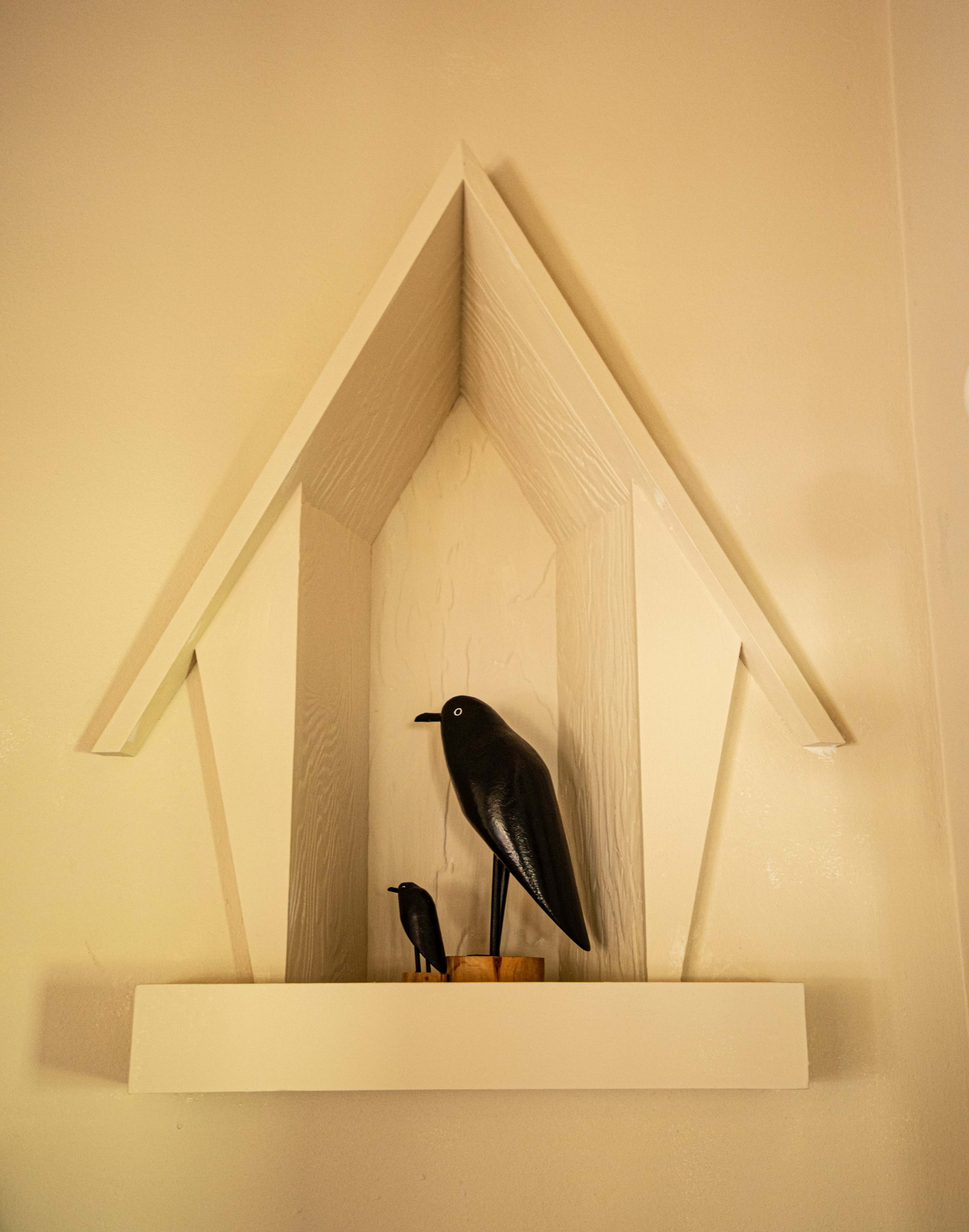A decorative wooden shelf in the shape of a house holds two black bird figurines.