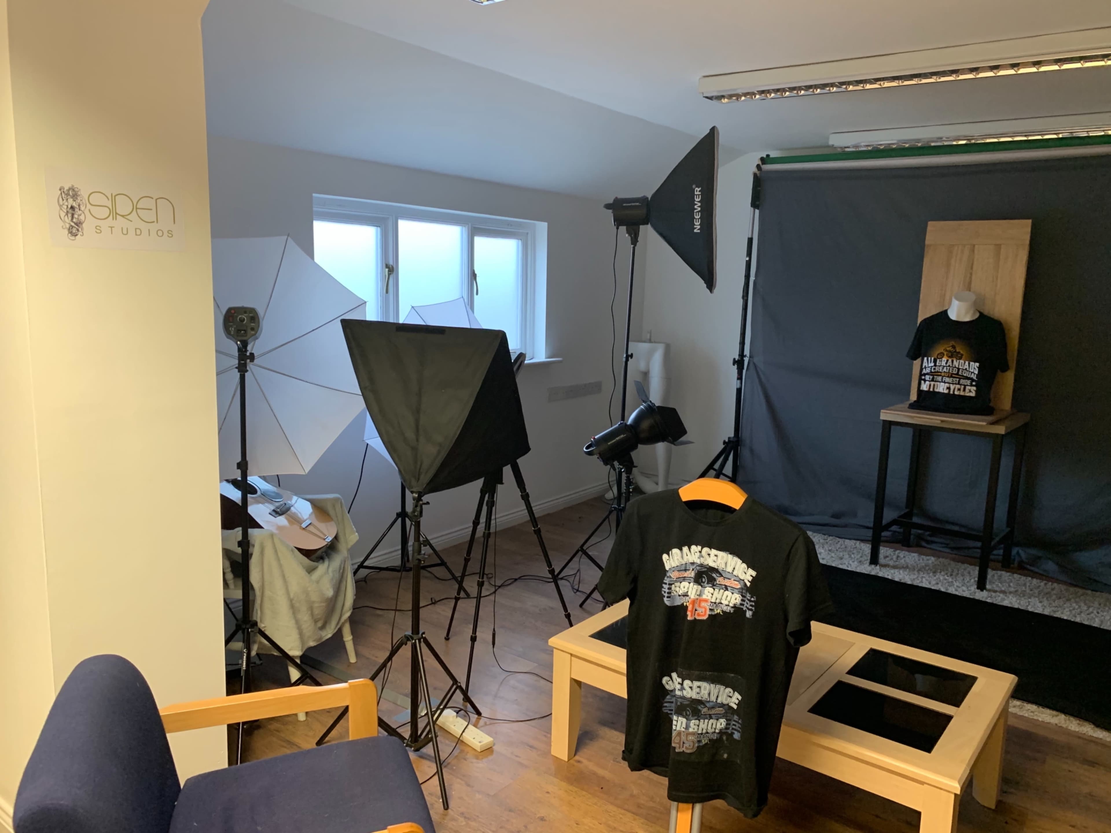 The image shows a photography studio setup with multiple lighting sources, a display mannequin wearing a T-shirt, and a backdrop.