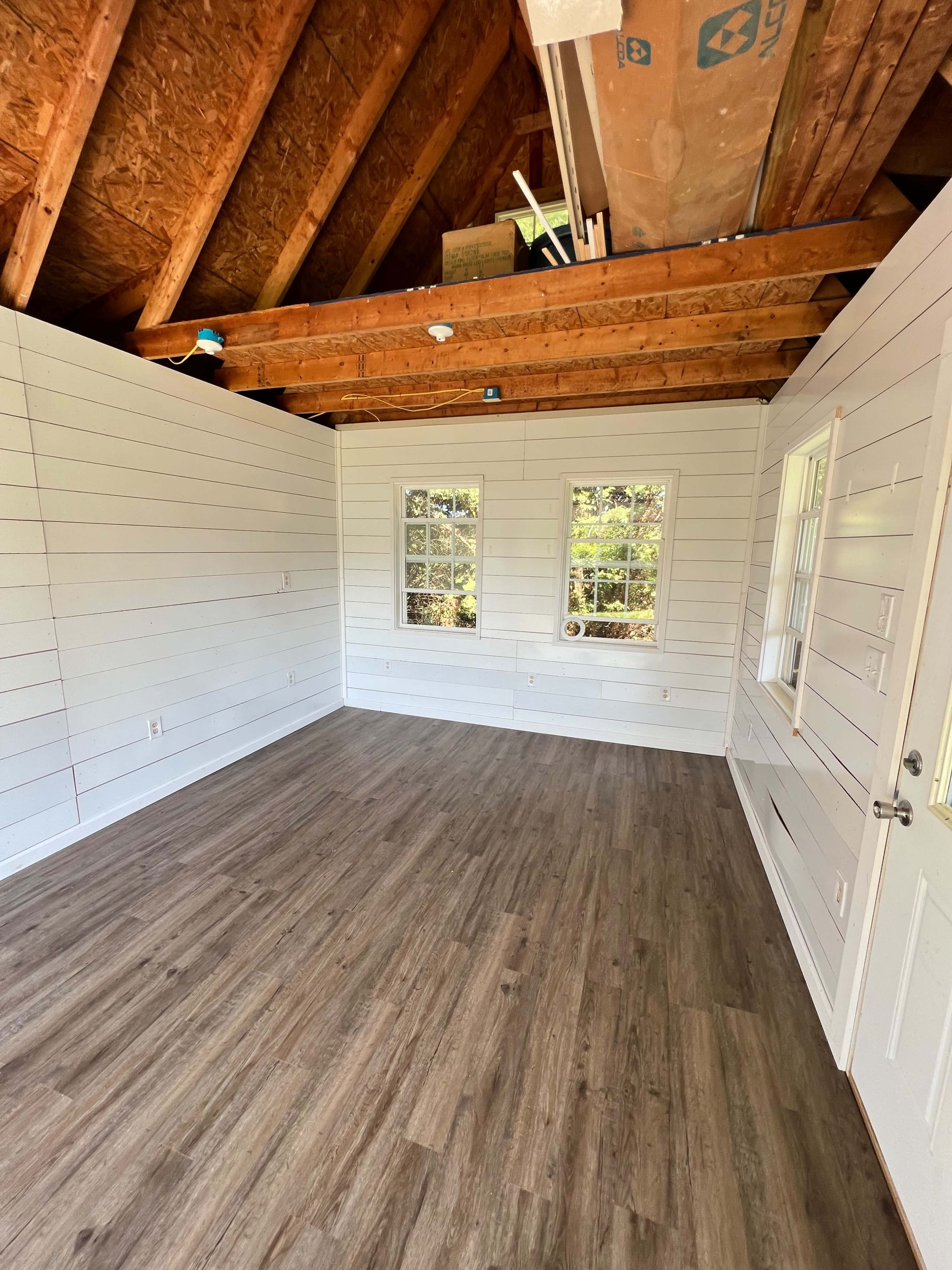 An empty room with wooden floors, white paneled walls, and exposed beams in the ceiling.