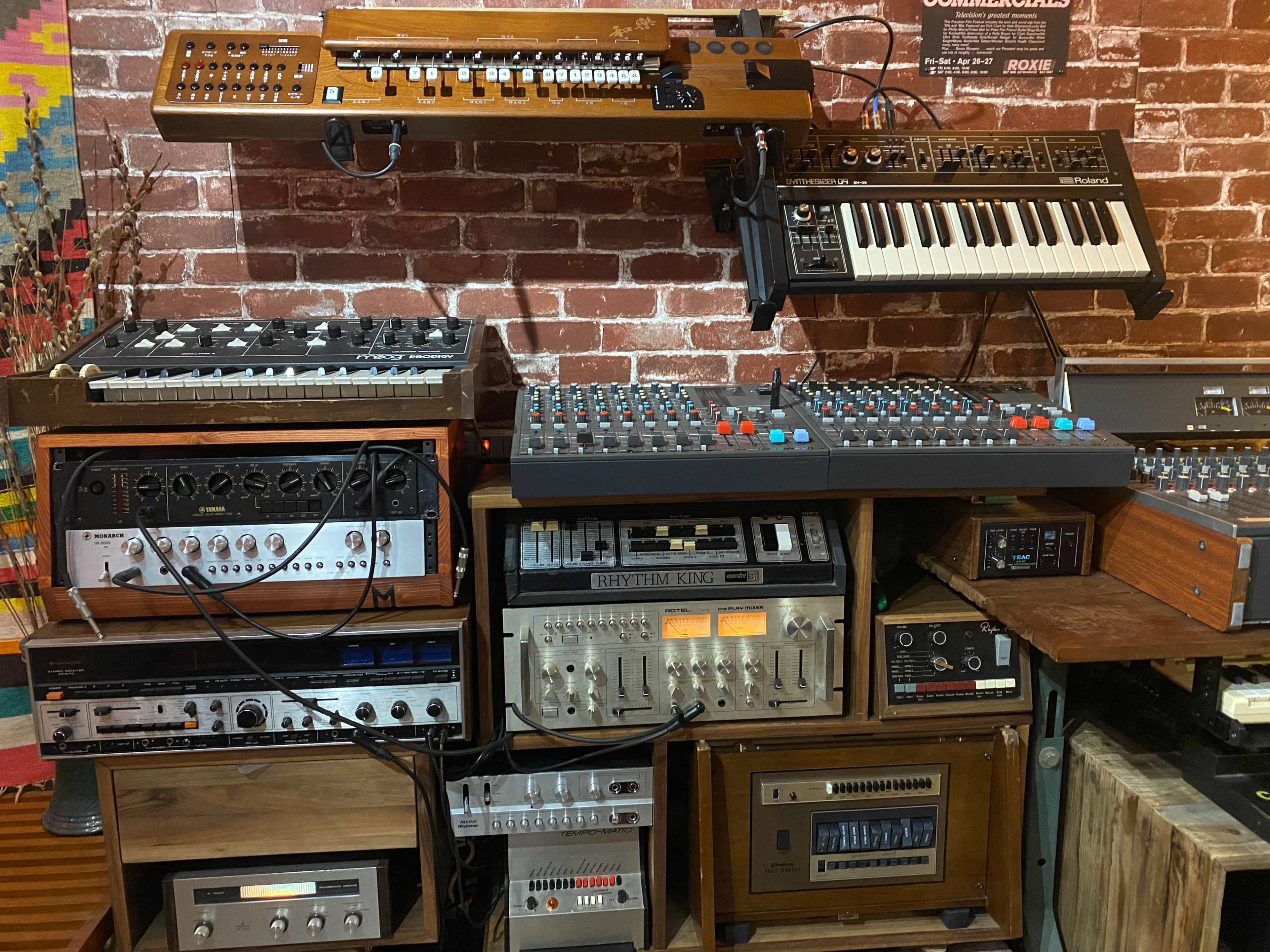 A collection of various vintage synthesizers and audio equipment arranged against a brick wall.