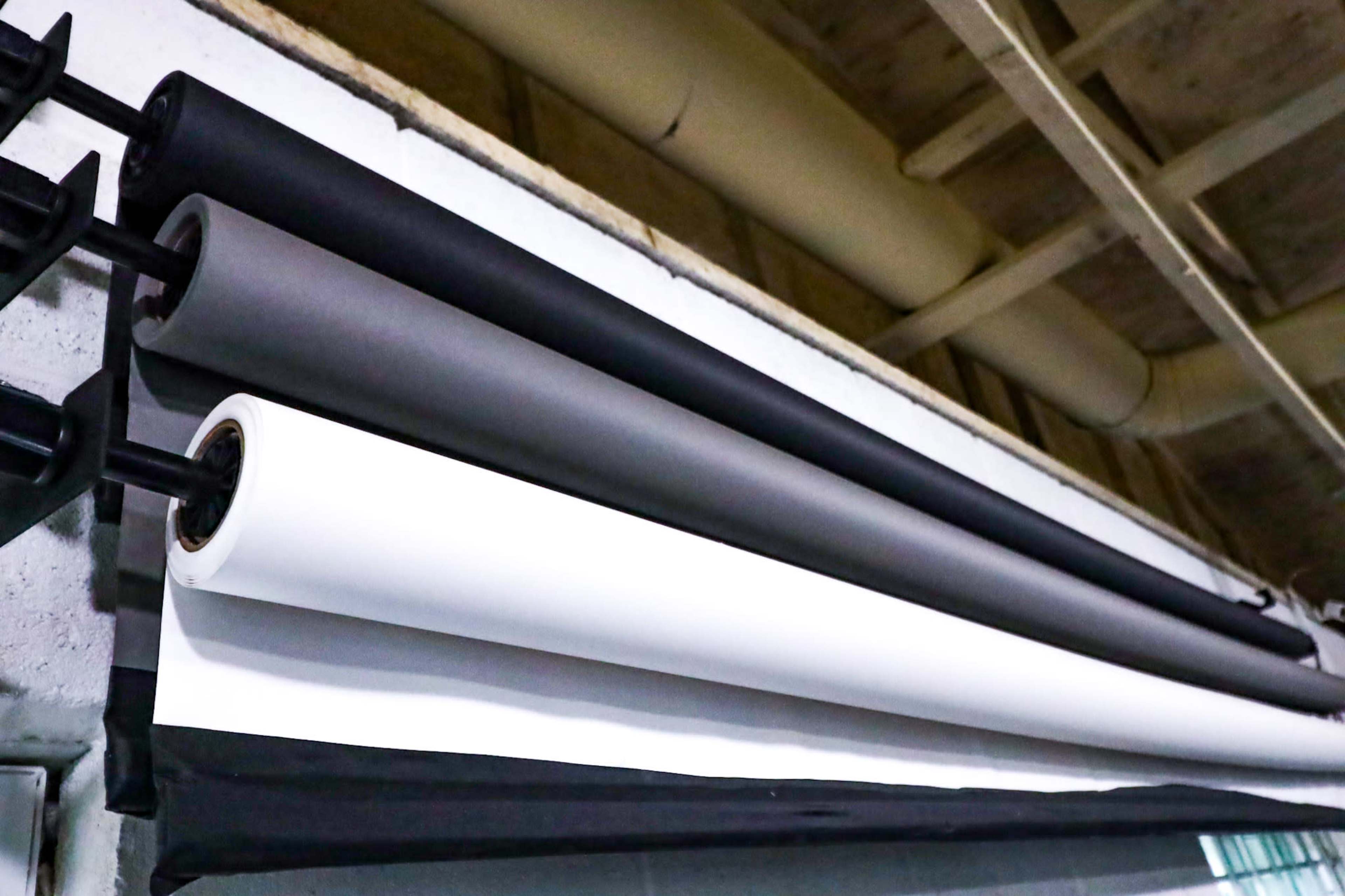 Four rolls of photography backdrop paper, in black, gray, and white, are mounted on a rack against a wall.