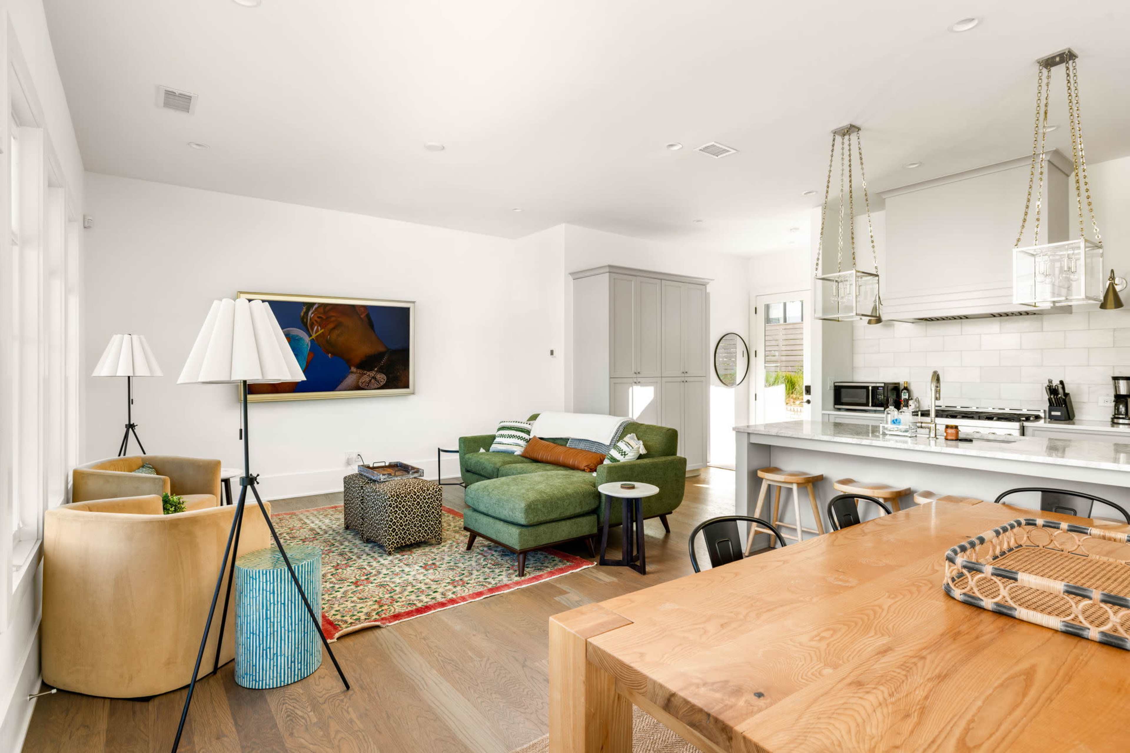 The image shows a modern, open-concept living space with a kitchen, dining area, and seating area featuring a green sofa and wooden dining table.