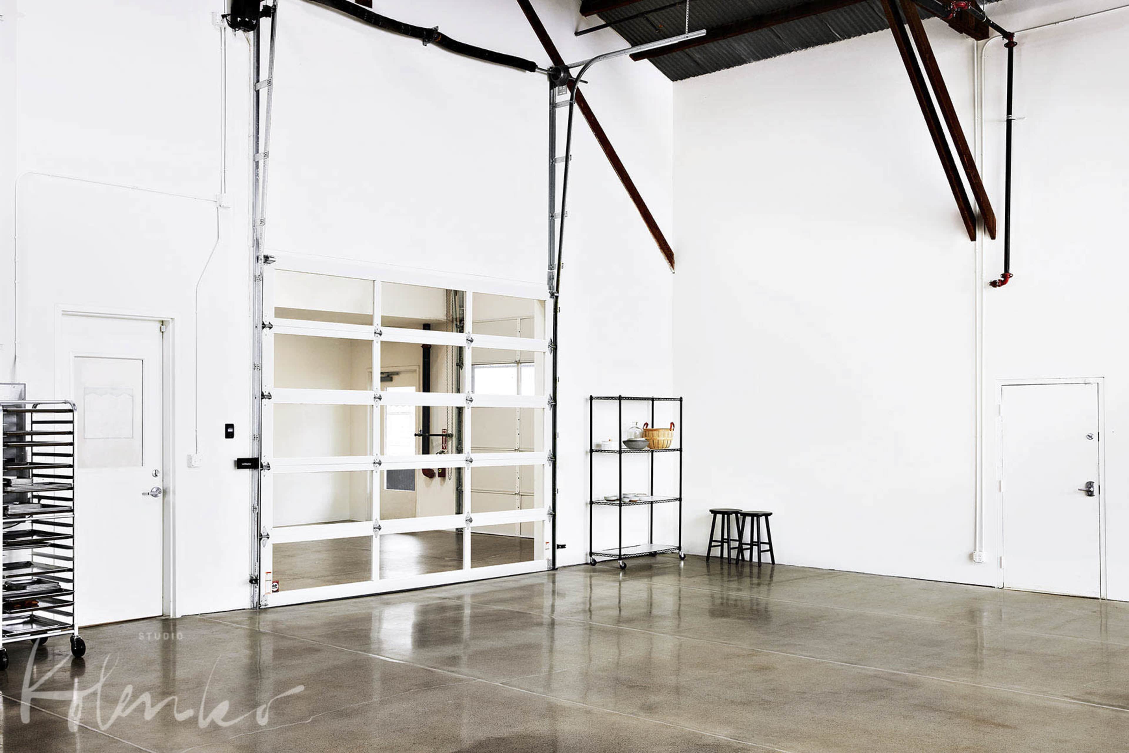 A spacious, empty room with concrete flooring, large windows, and minimal furnishings.
