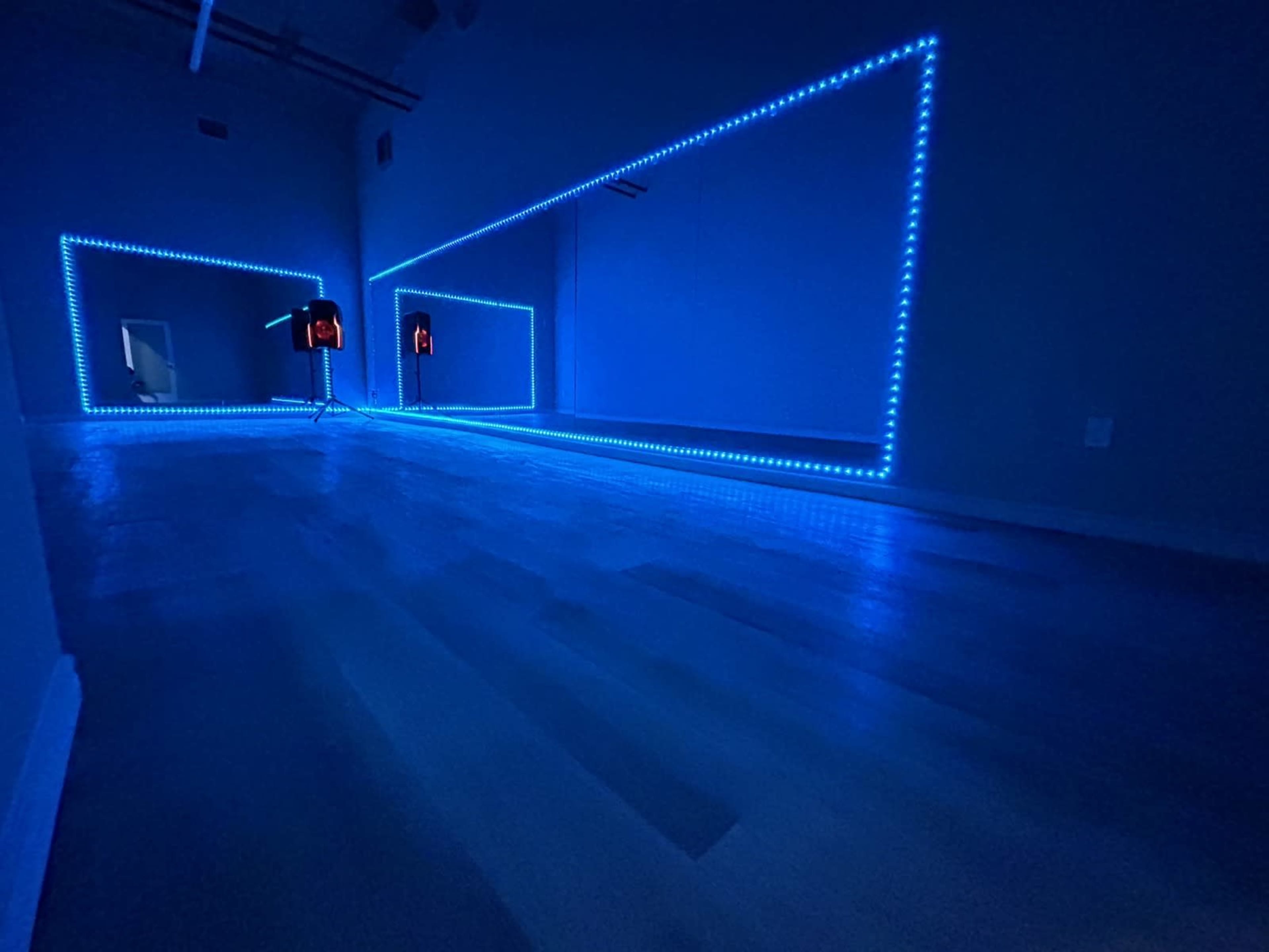 The image shows a dimly lit room with blue LED lights outlining two large mirrors on opposite walls.