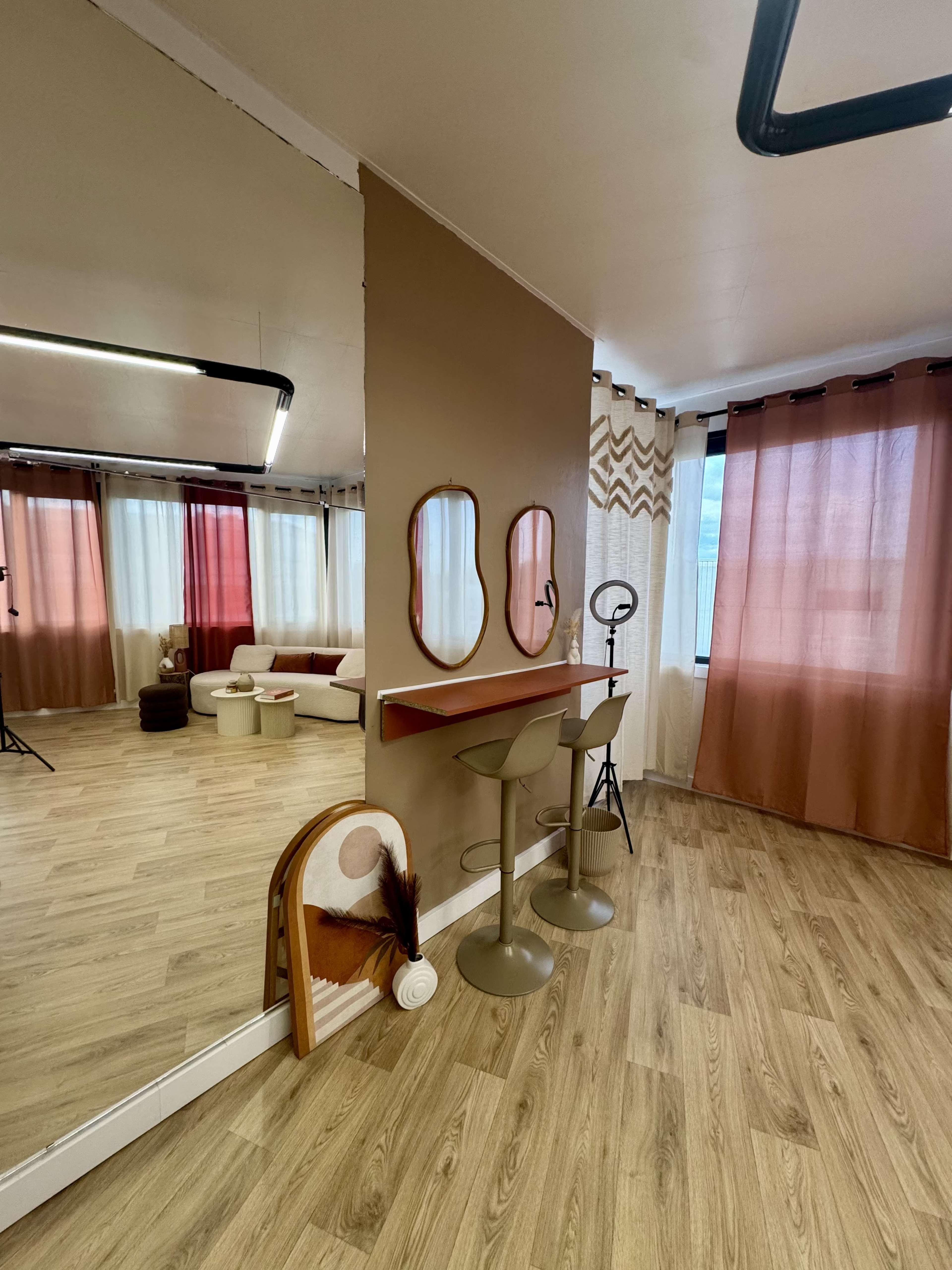 The image shows a modern interior with a reflection in a mirror, featuring a seating area, bar stools, and large windows with sheer curtains.