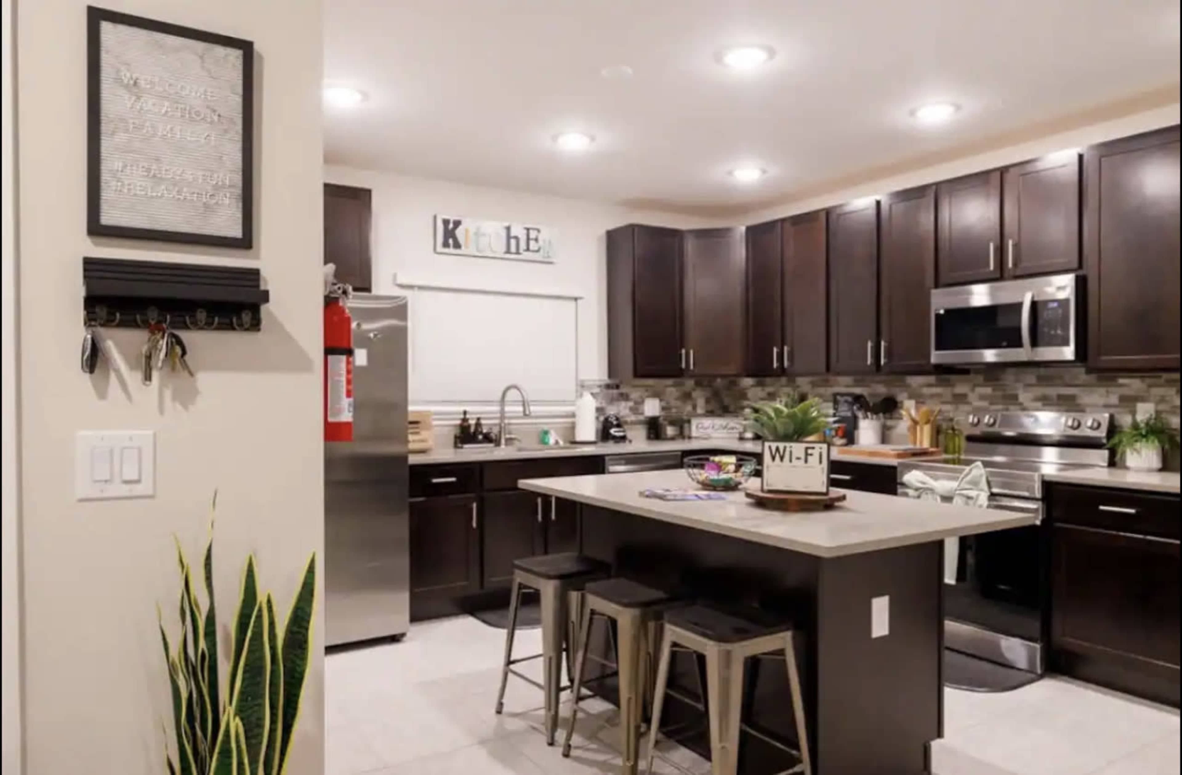 A modern kitchen featuring dark wooden cabinets, stainless steel appliances, and a central island with metal stools.