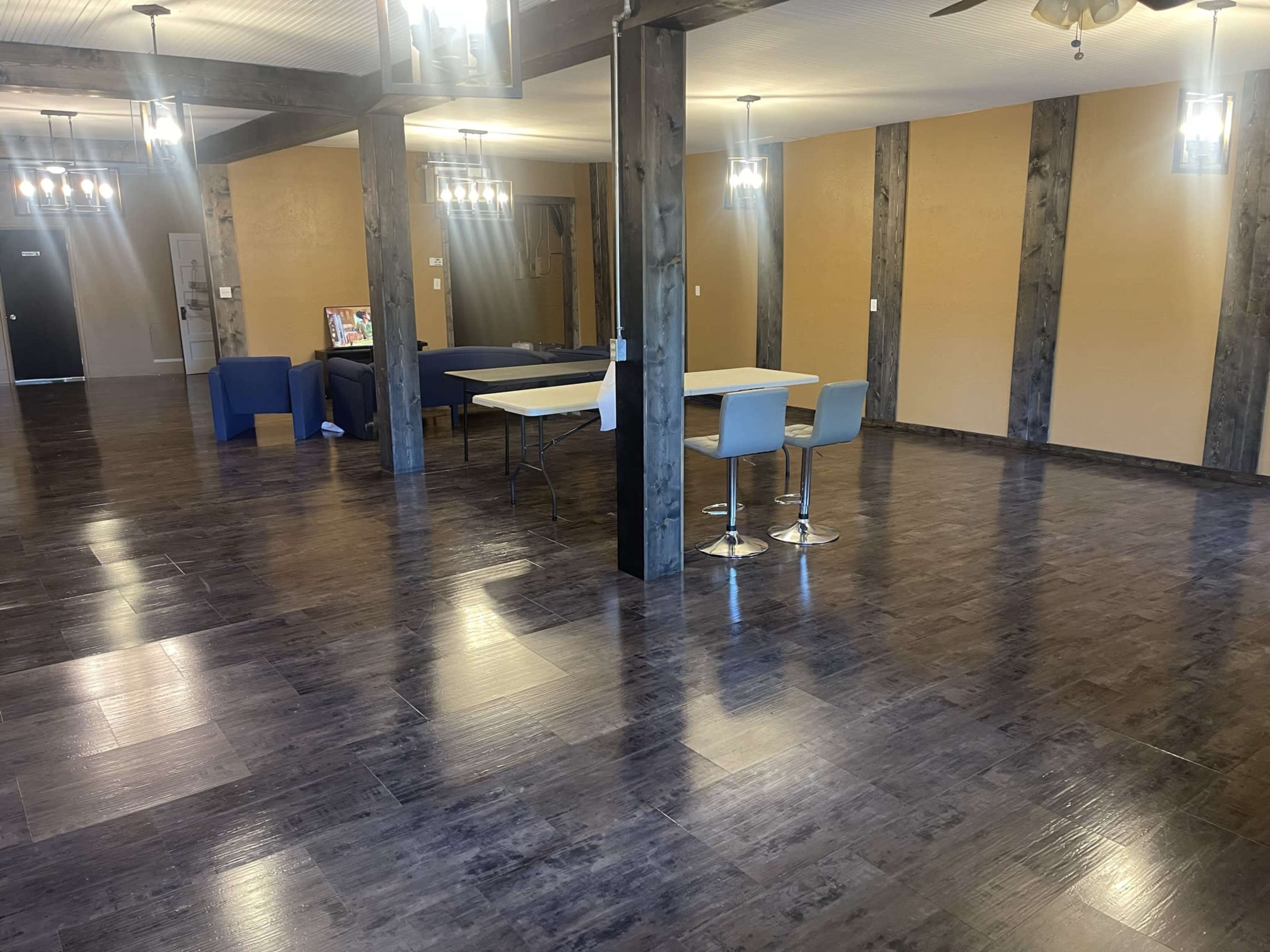 A spacious interior with hardwood flooring, featuring a table and chairs in the center and seating areas against the walls.