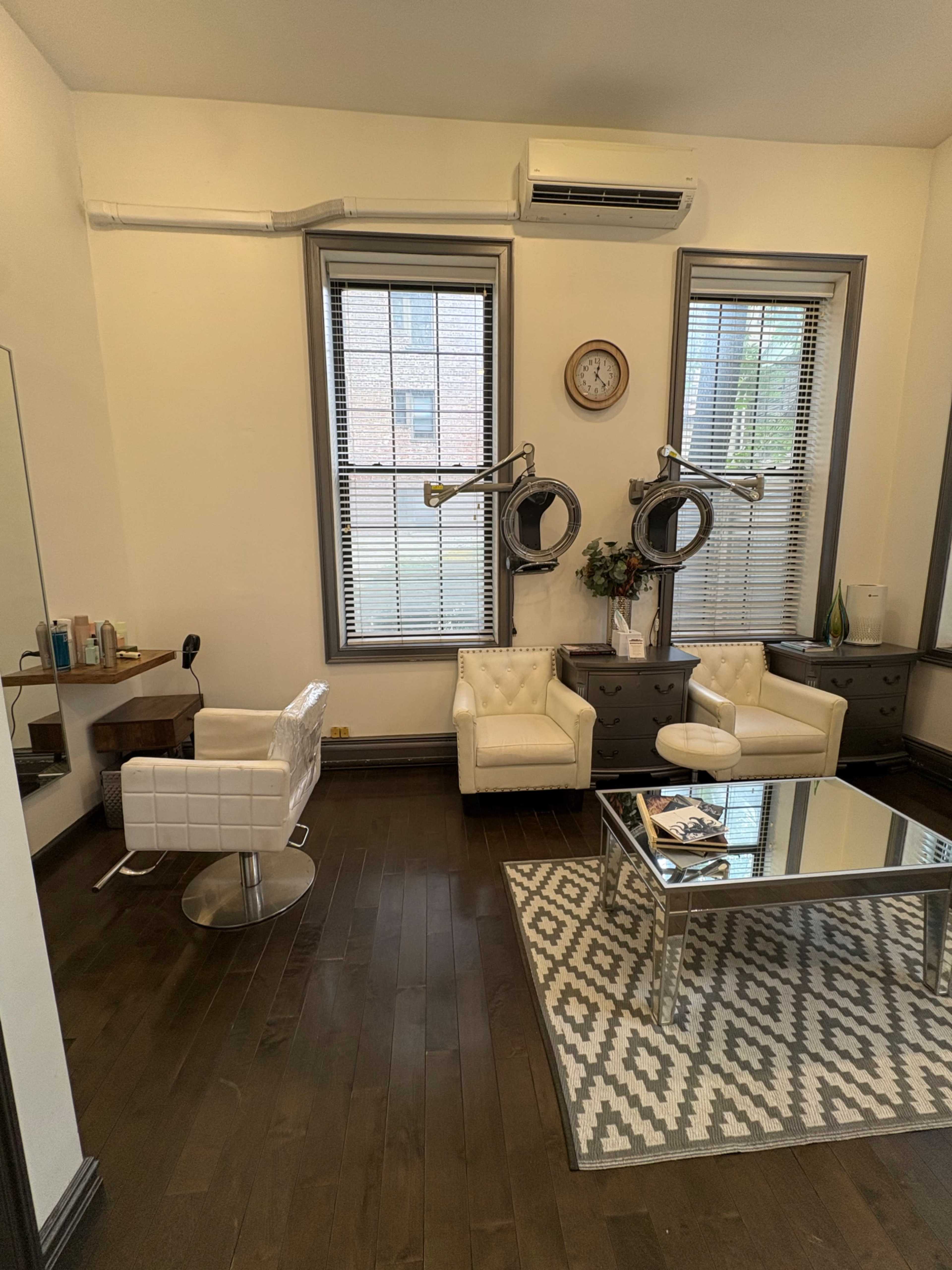 The image shows a modern hair salon interior with two white leather chairs, a glass table, decorative wall mirrors, and large windows letting in natural light.