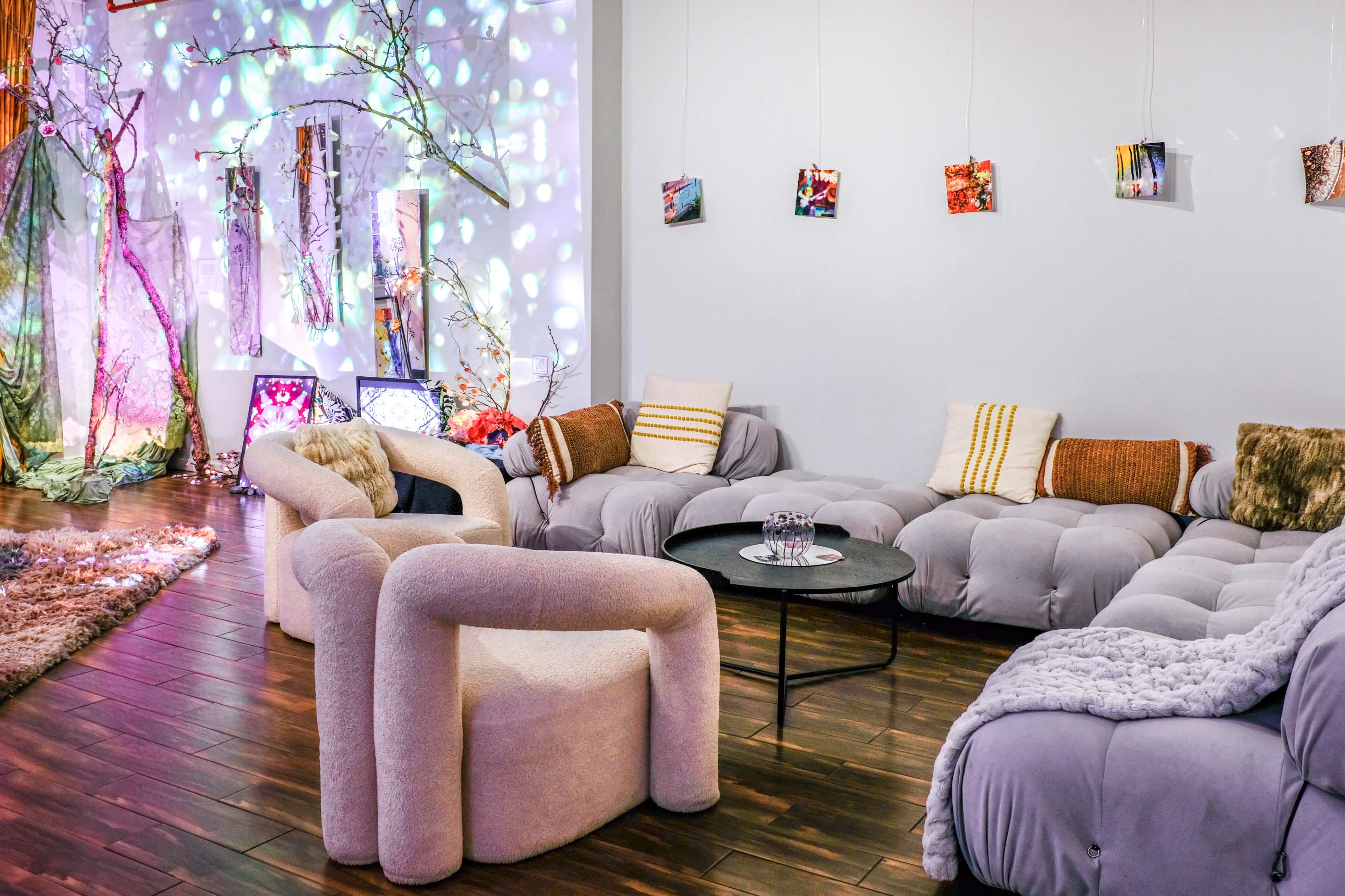 The image shows a modern lounge area with soft seating, a round black coffee table, and colorful wall decorations.
