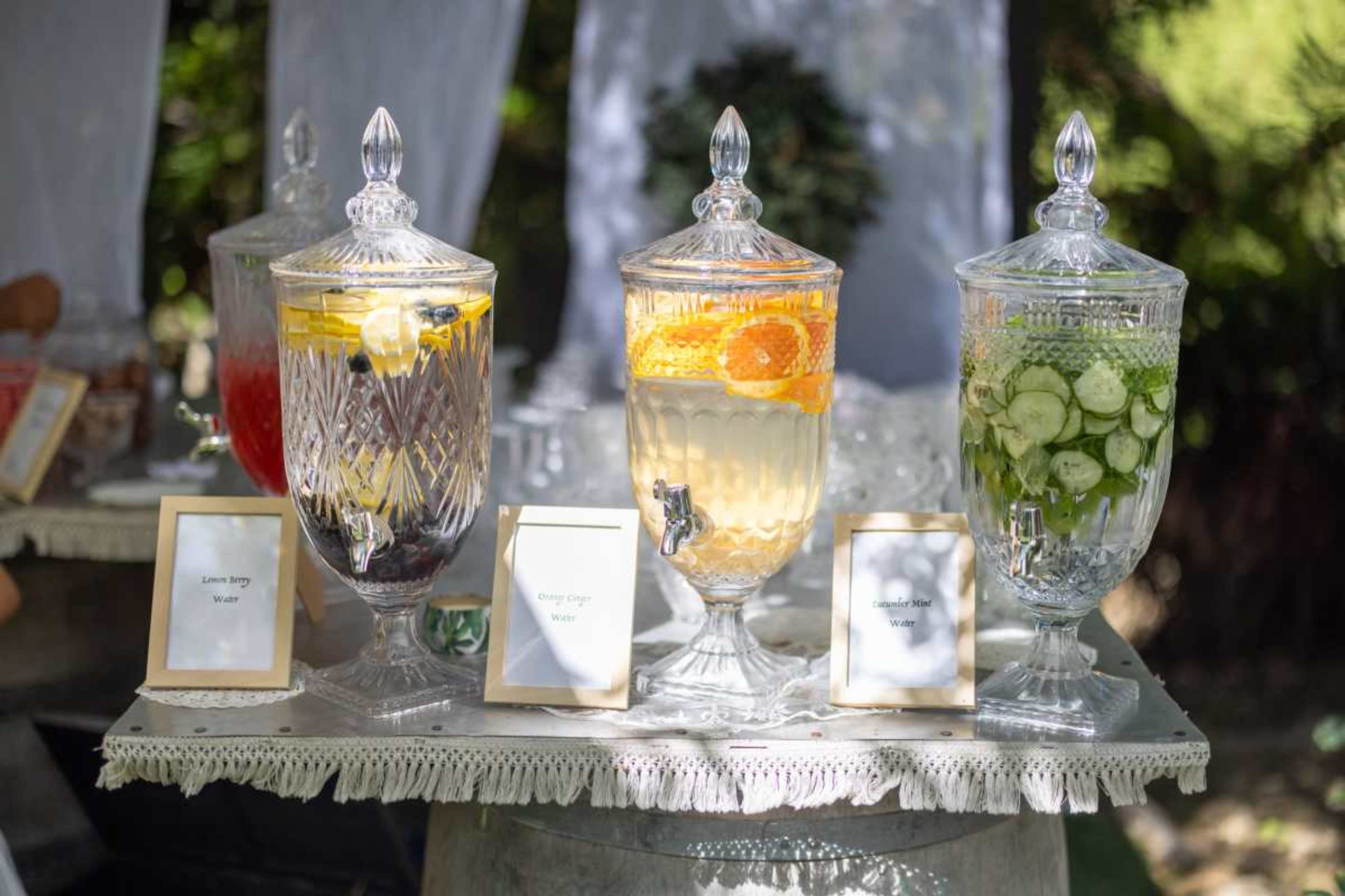 The image shows three glass beverage dispensers filled with colorful infused waters, each labeled with a different flavor.
