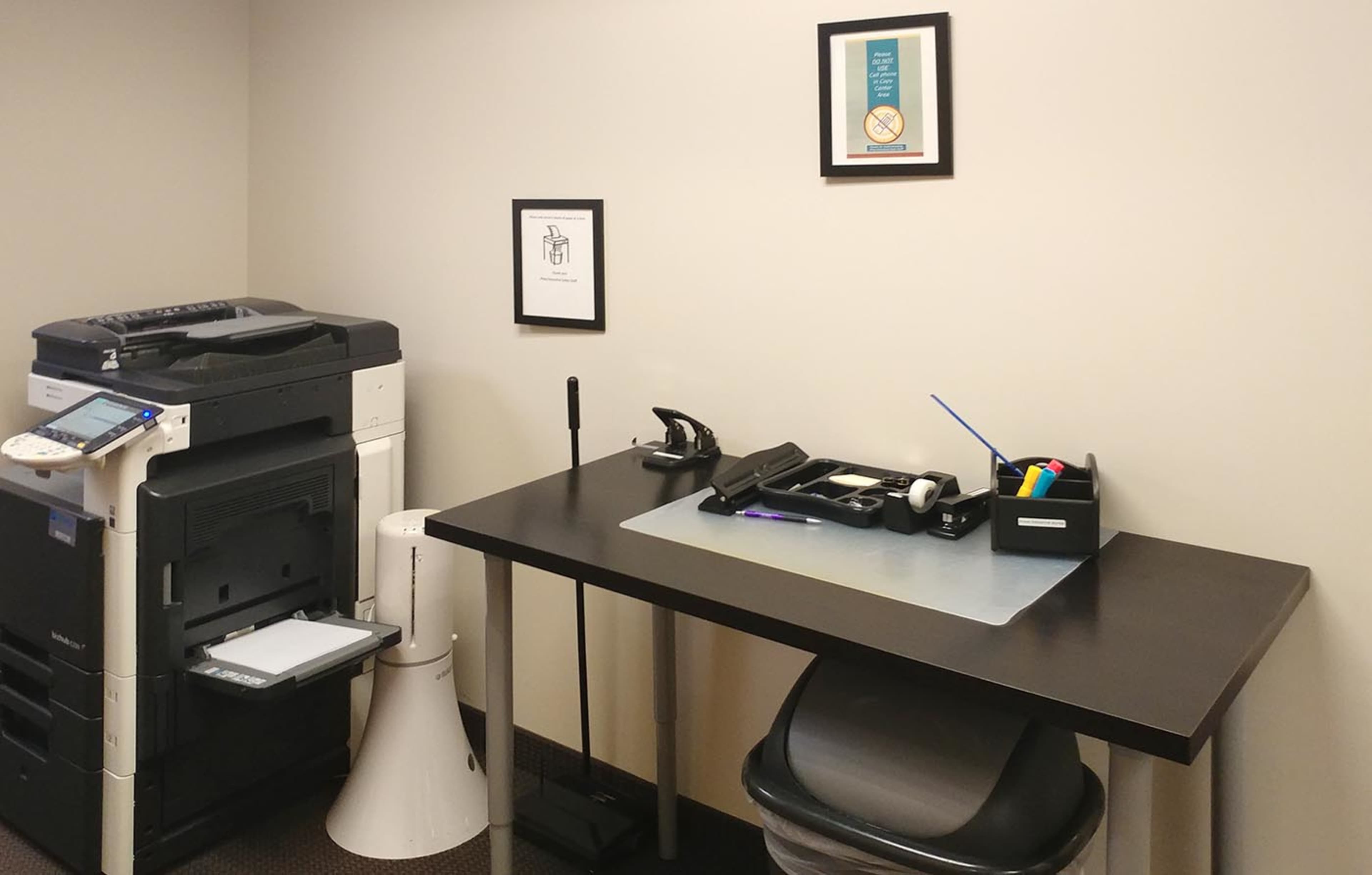 A workspace features a printer, a desk with office supplies, and framed posters on the wall.