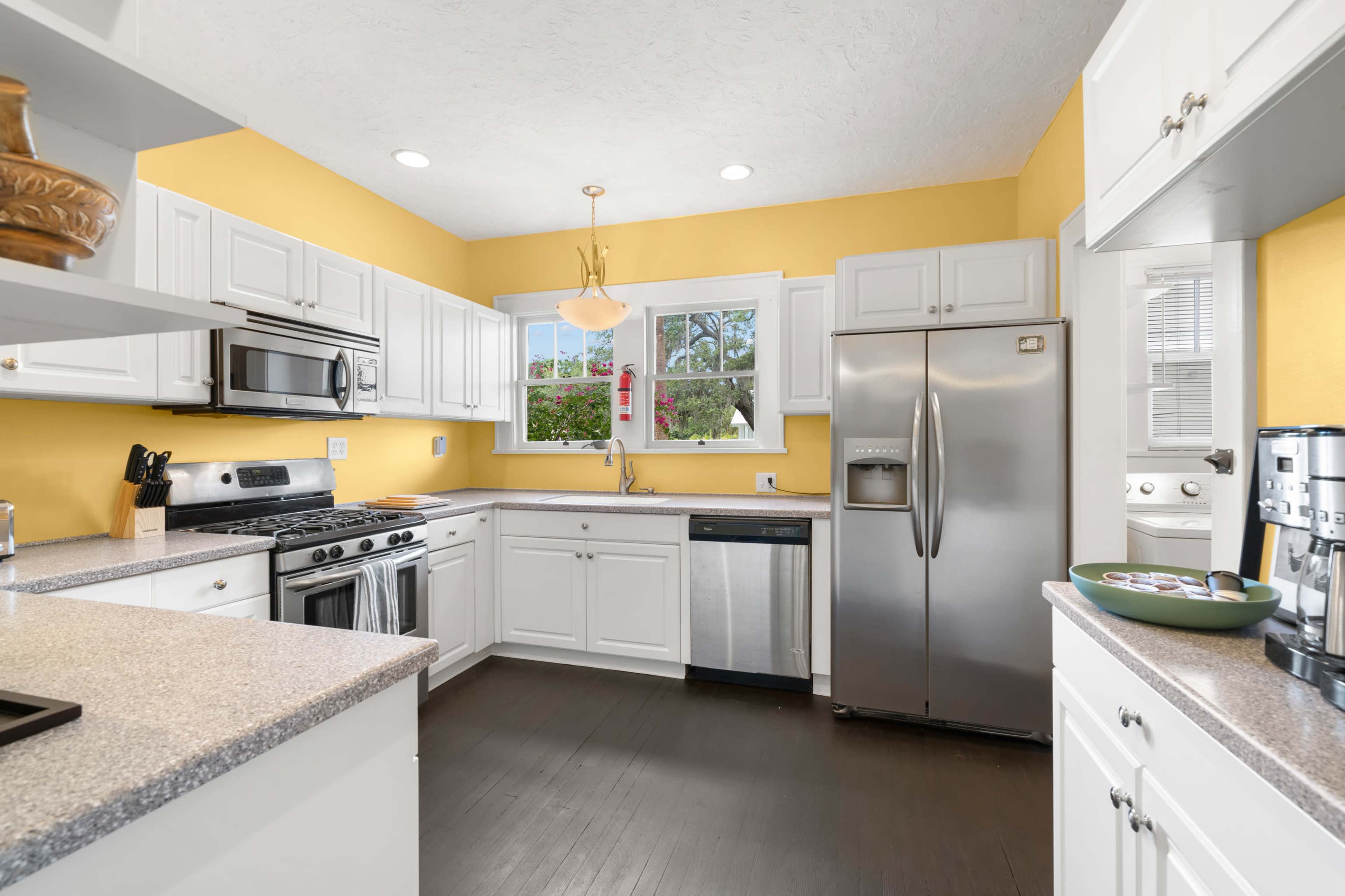 The kitchen features white cabinetry, stainless steel appliances, and yellow walls with a view out of the window.