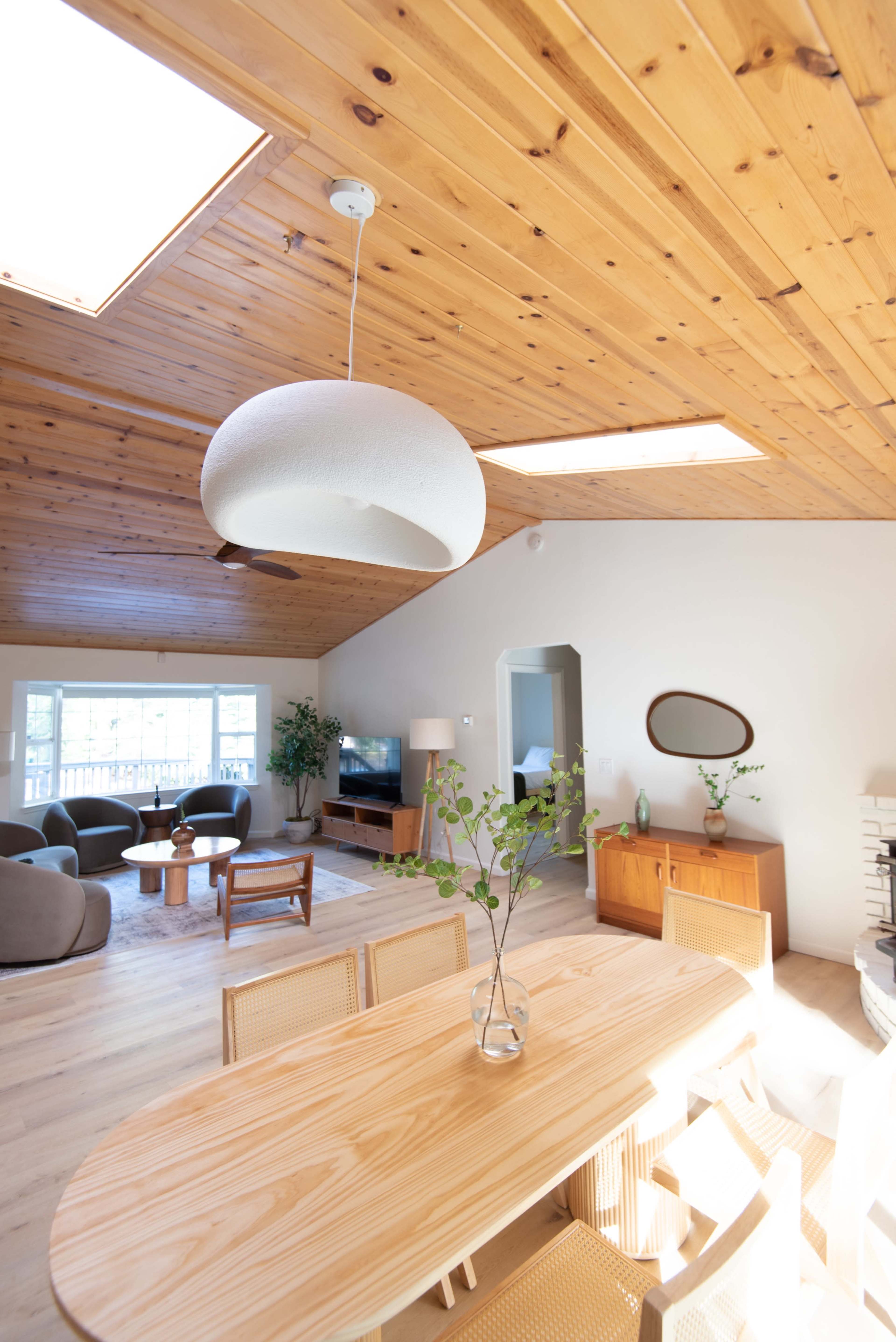 A modern, open-concept living space featuring a wooden ceiling, large windows, a dining table, and various seating arrangements.