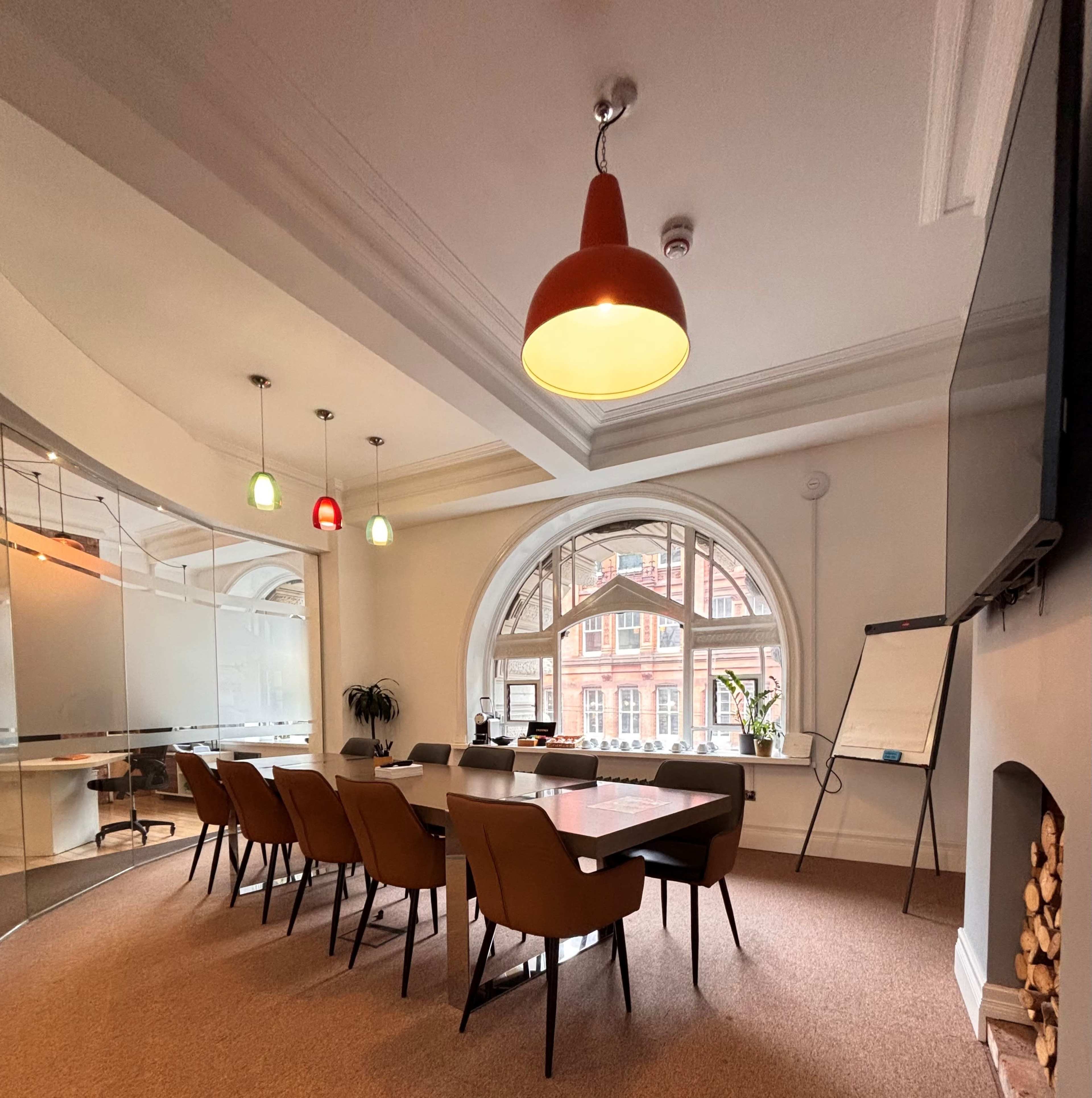 The image shows a modern conference room with a large table surrounded by chairs, featuring a curved window and a wall-mounted TV.