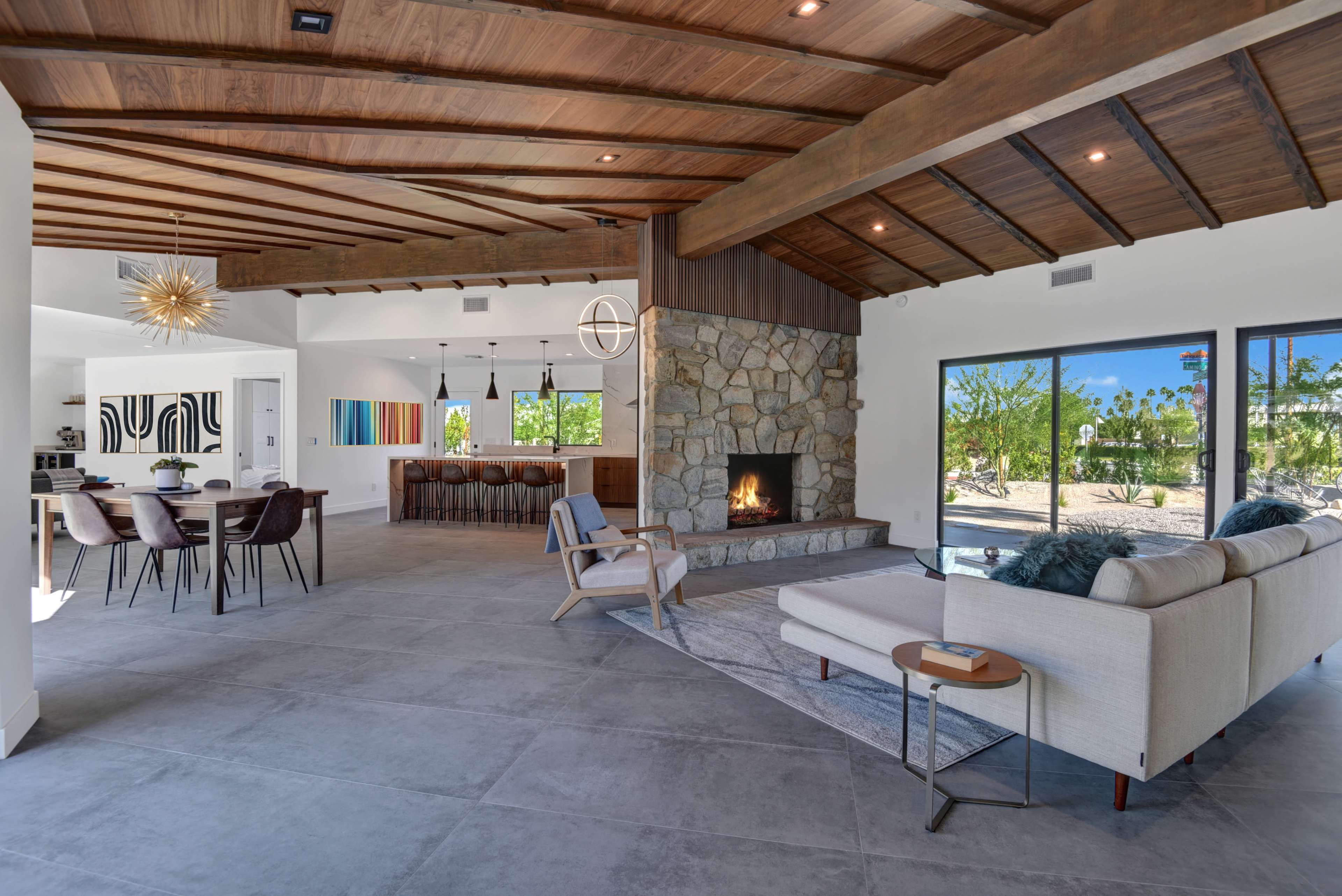 The modern interior features a spacious living area with a stone fireplace, wooden beams, and large windows overlooking a patio.