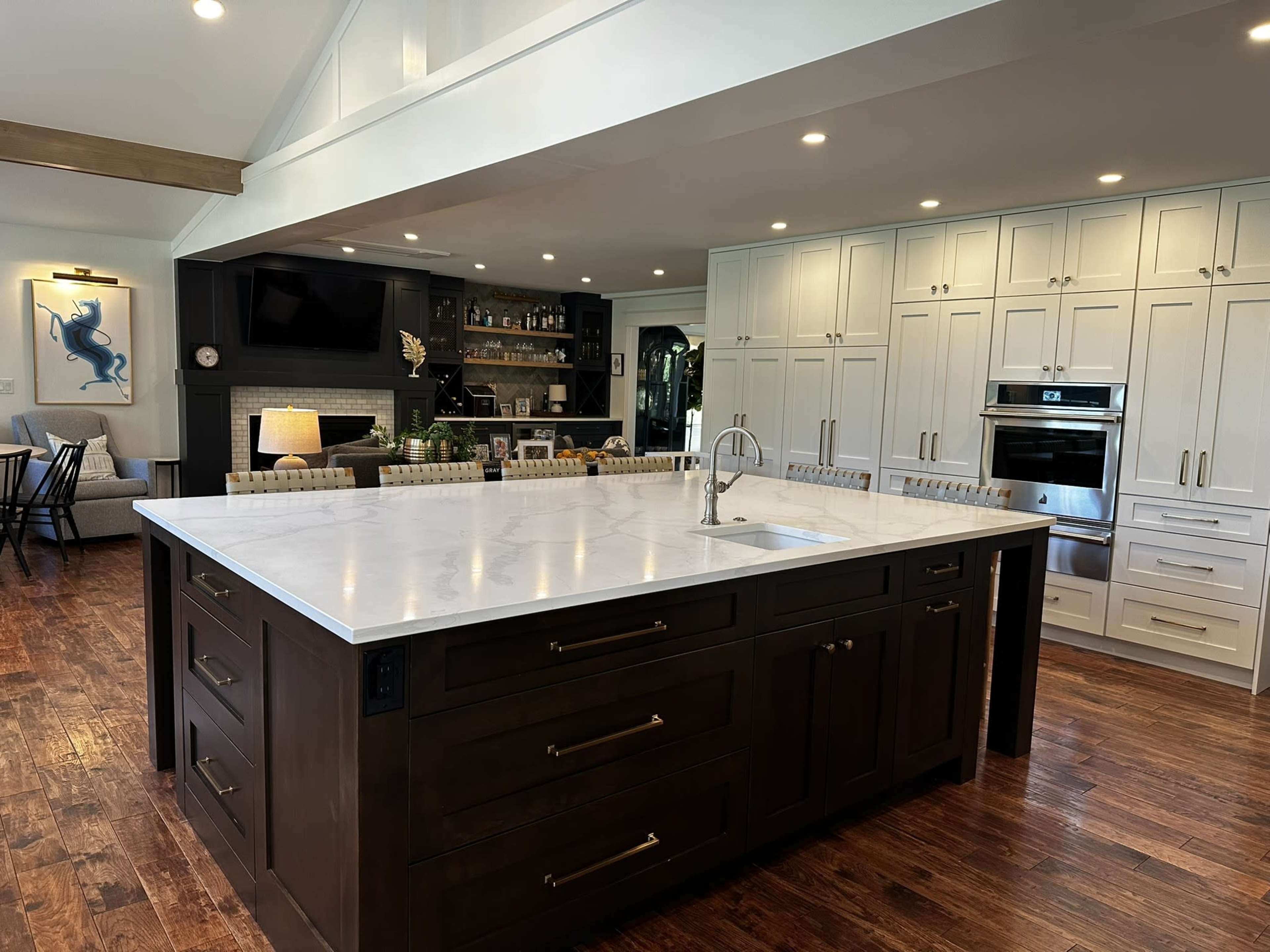 The kitchen features a large central island with a white marble countertop, dark cabinetry, and modern appliances, surrounded by white cabinets and hardwood flooring.