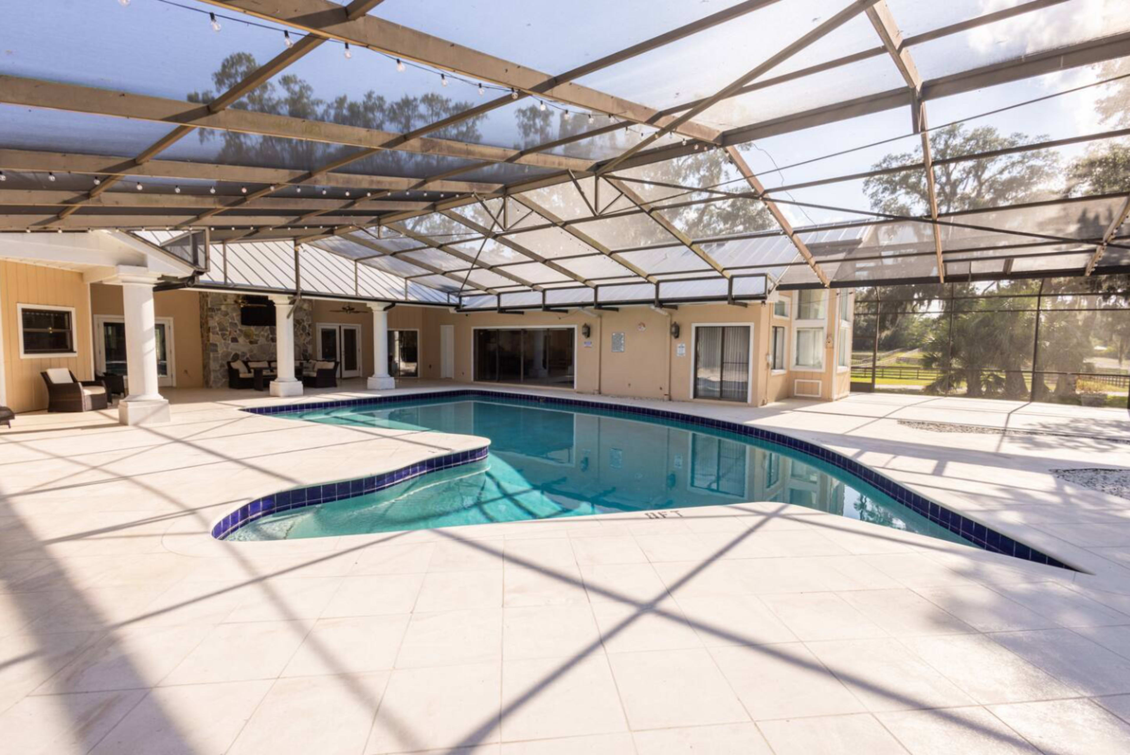 The image shows a screened-in swimming pool area with a tiled pool, surrounded by a patio and adjacent covered spaces.