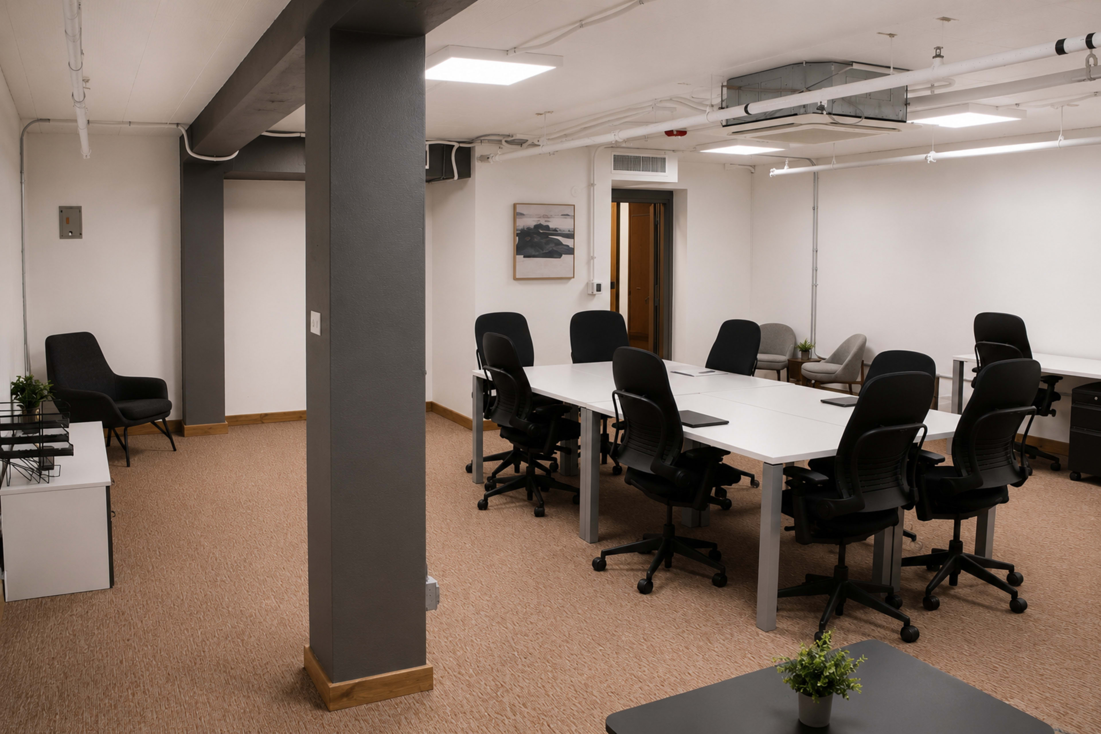 The image shows a modern office space with a large table surrounded by black office chairs and minimalistic furnishings.