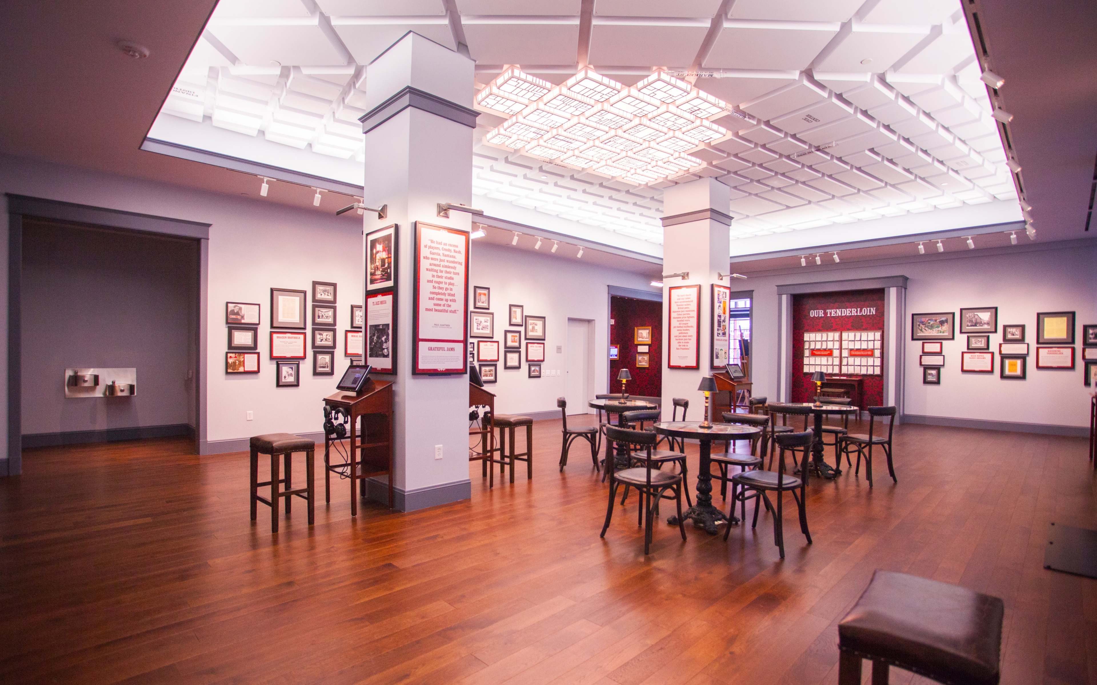 An interior view of a museum exhibit featuring wooden tables and chairs arranged around a space with framed photographs and documents on the walls.