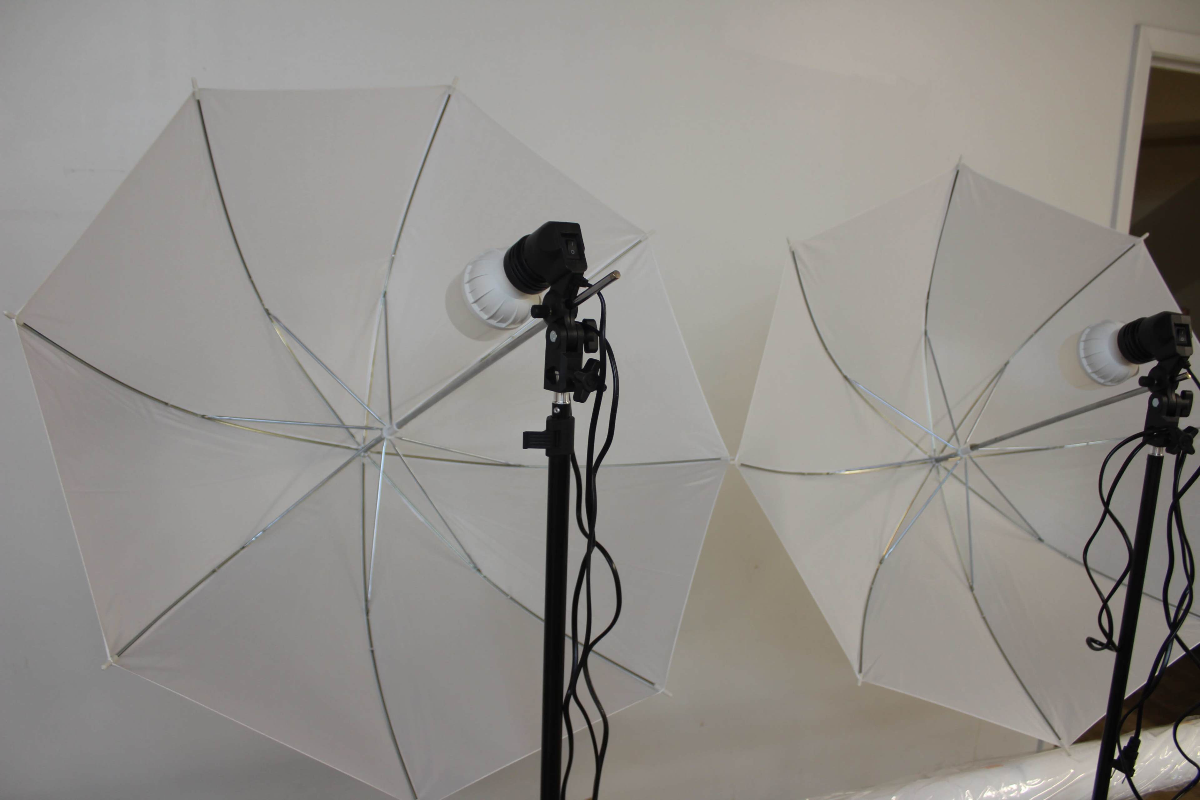The image shows two large white softbox umbrellas positioned on stands, with a light source attached to one of the stands.