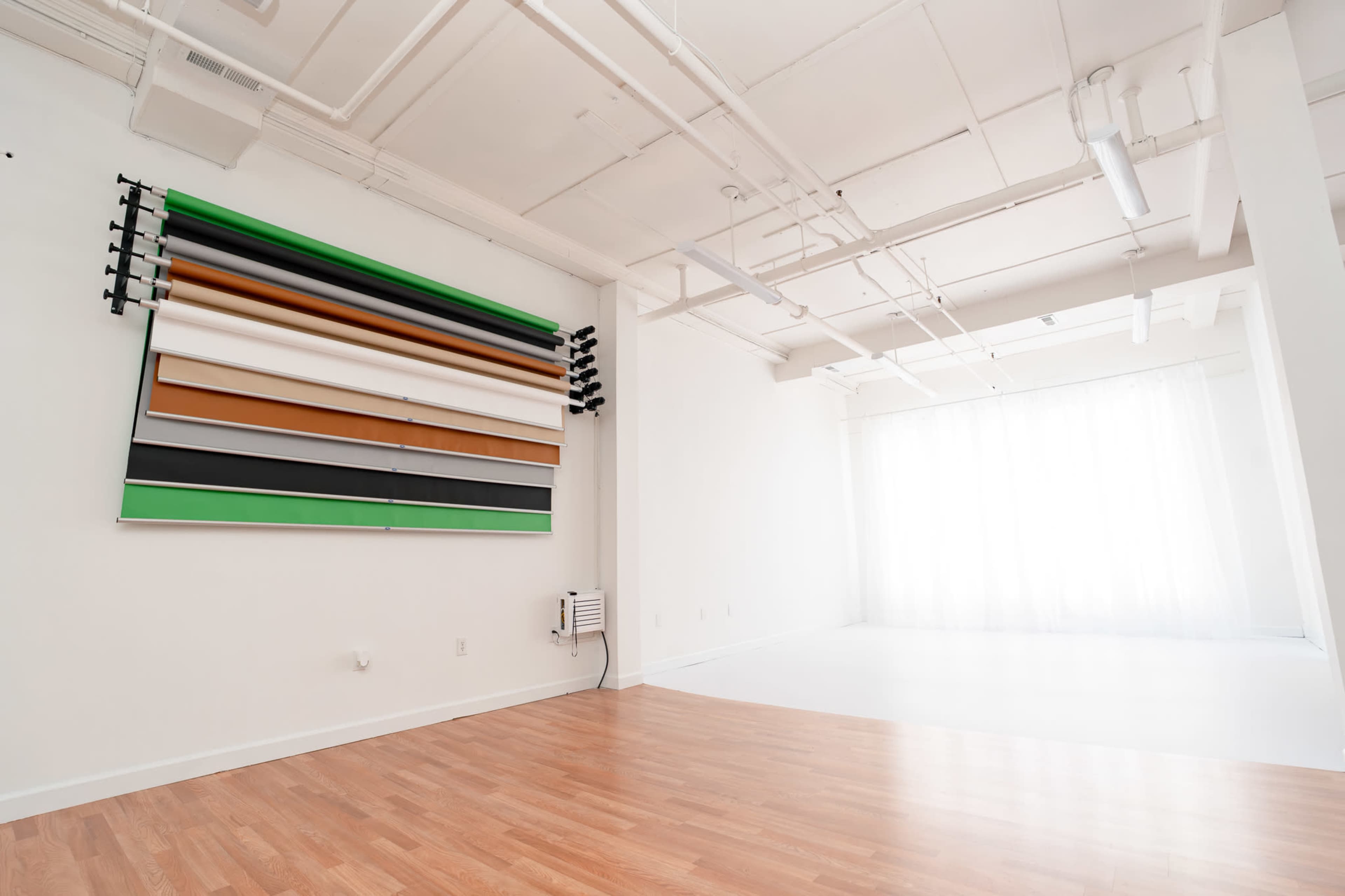 The image shows a spacious, well-lit studio with a wall displaying colored backdrops and a section with a white curtain.
