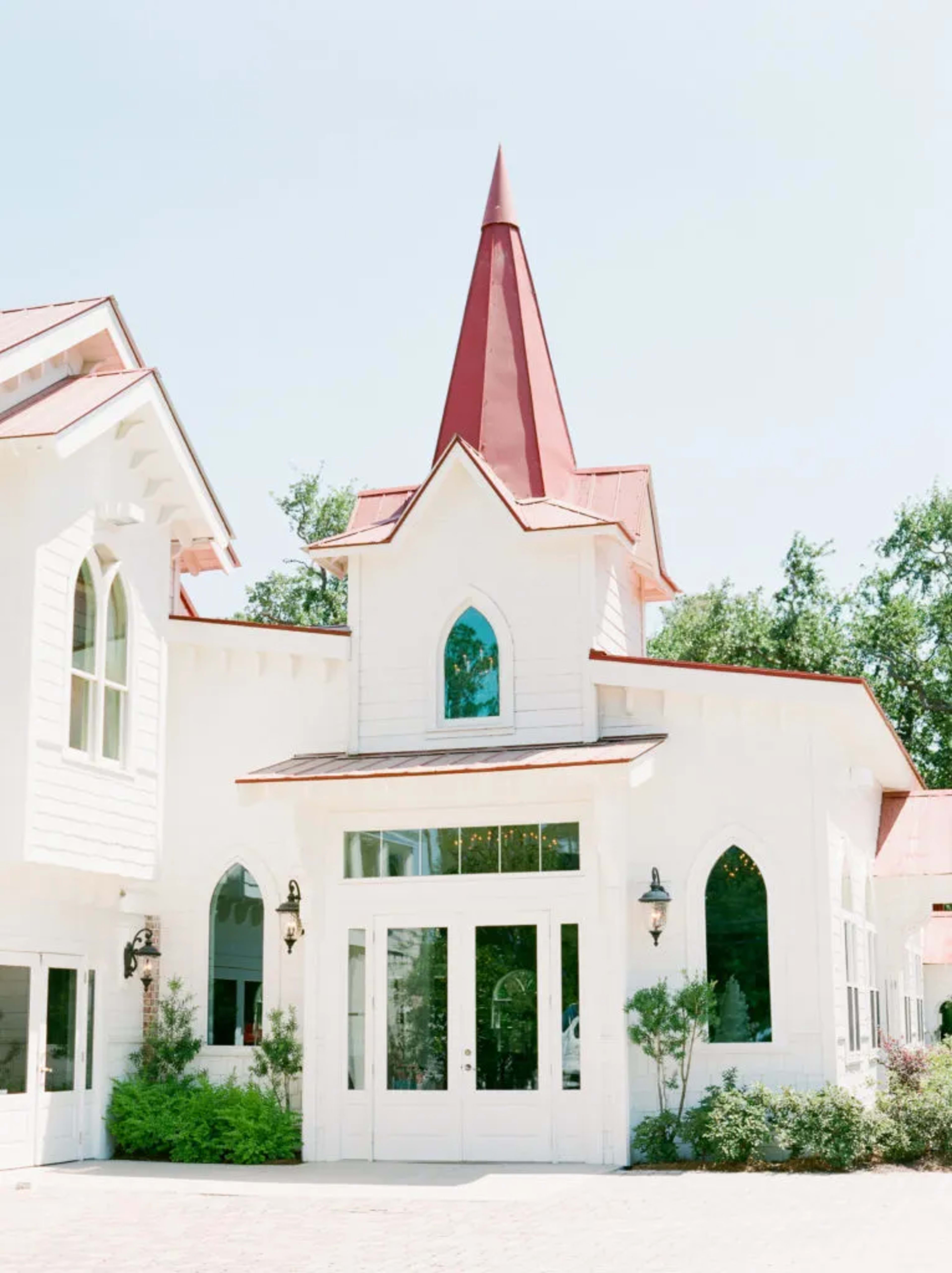 The image shows a white building with a tall, red spire and arched windows.