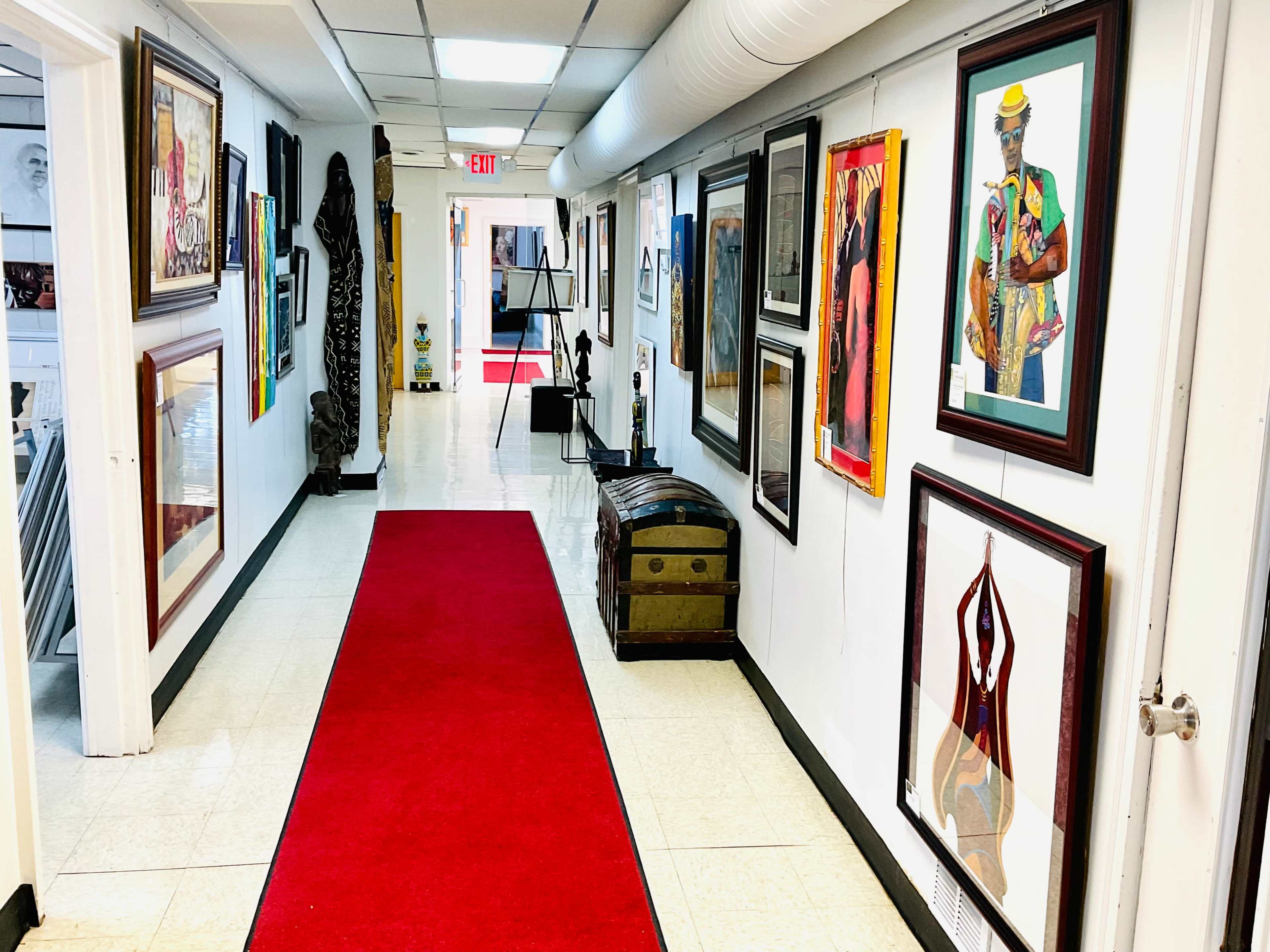 A long hallway features a red carpet and various framed artworks on the walls, with decorative items placed along the sides.