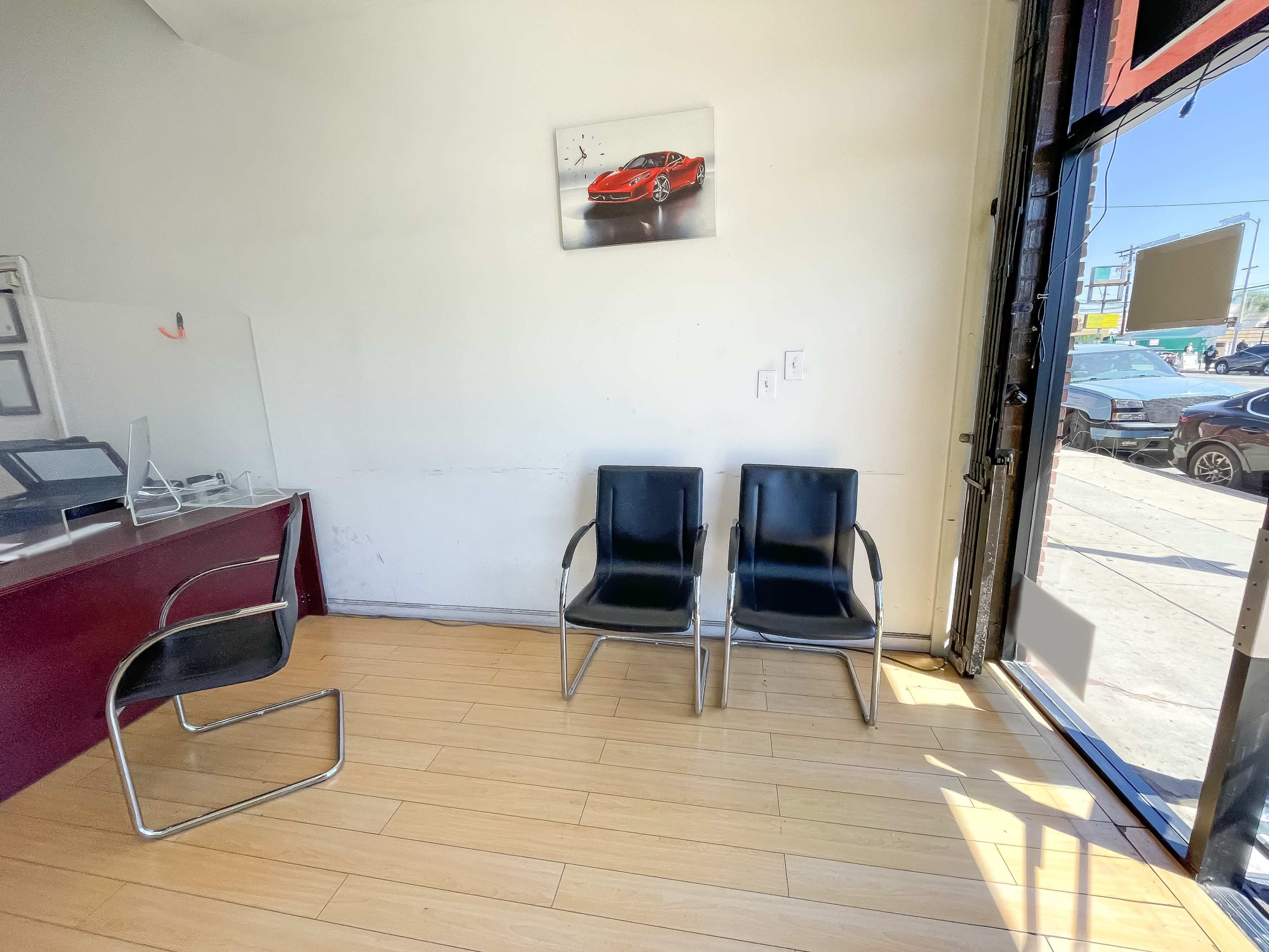 The image shows a small waiting area with two black chairs and a wall-mounted picture of a red car.
