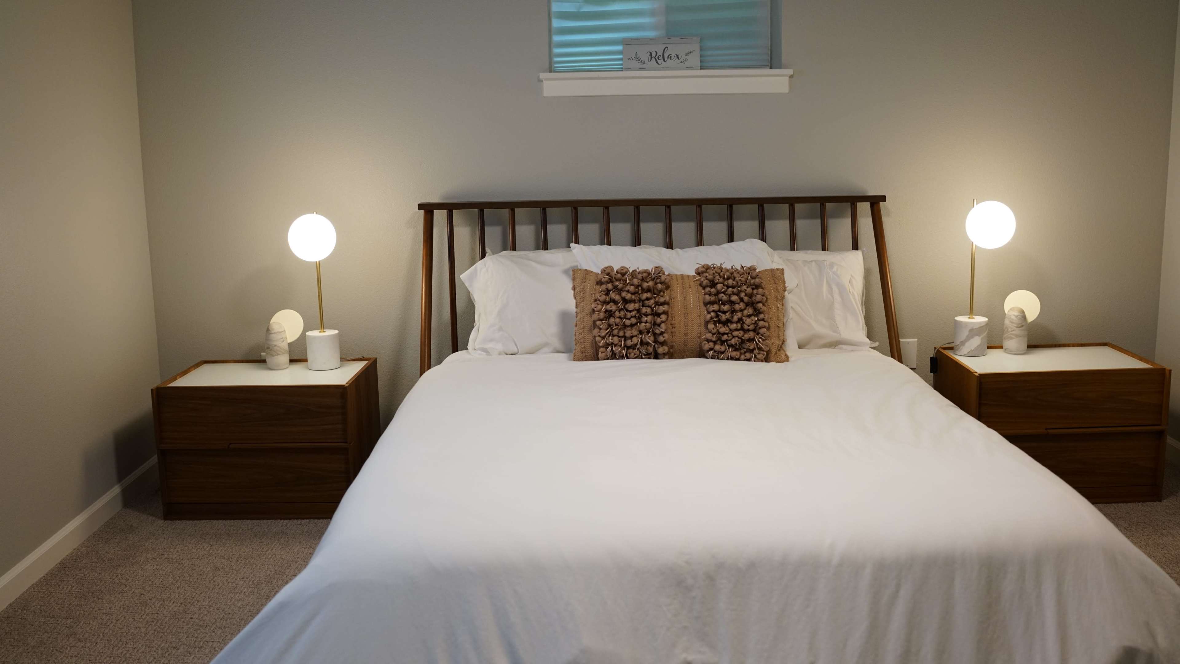 A neatly made bed with a wooden headboard is centered in a softly lit bedroom, flanked by two nightstands with modern lamps.