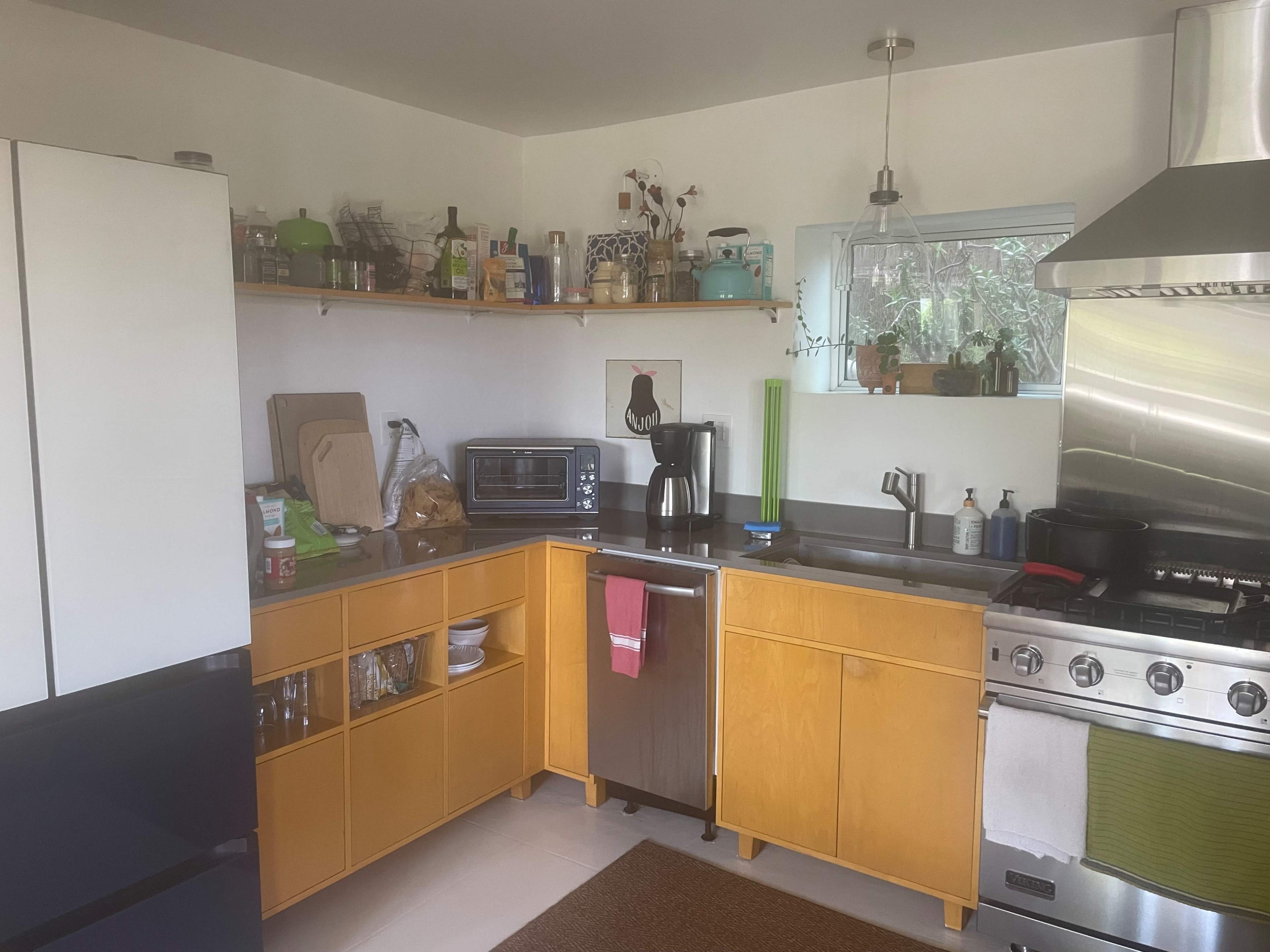 The kitchen features wooden cabinets, a stainless steel sink, and appliances including a microwave and a gas stove, with shelves holding various kitchen items.