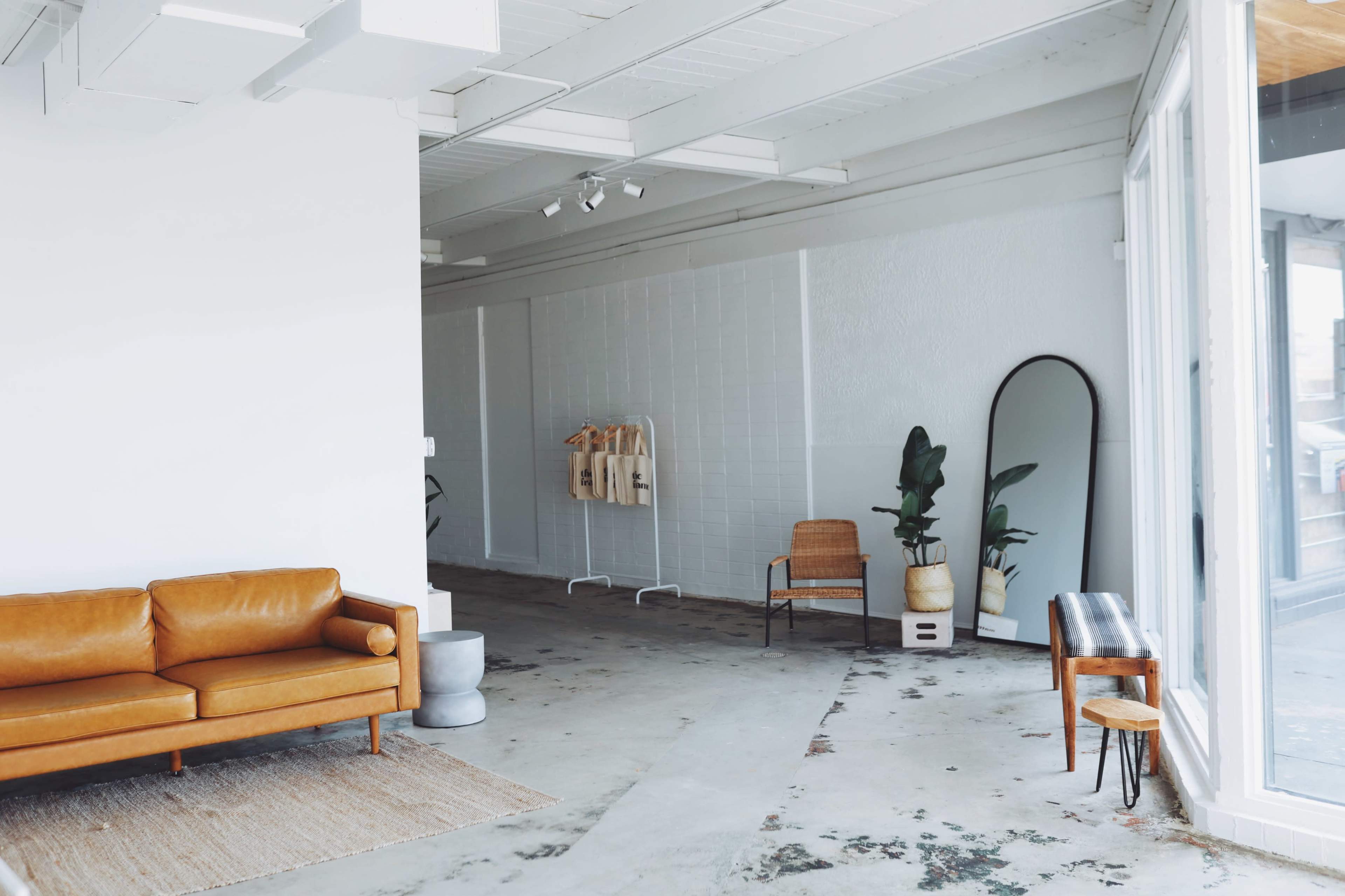 A spacious interior with a brown leather sofa, a large mirror, a rattan chair, and several potted plants.