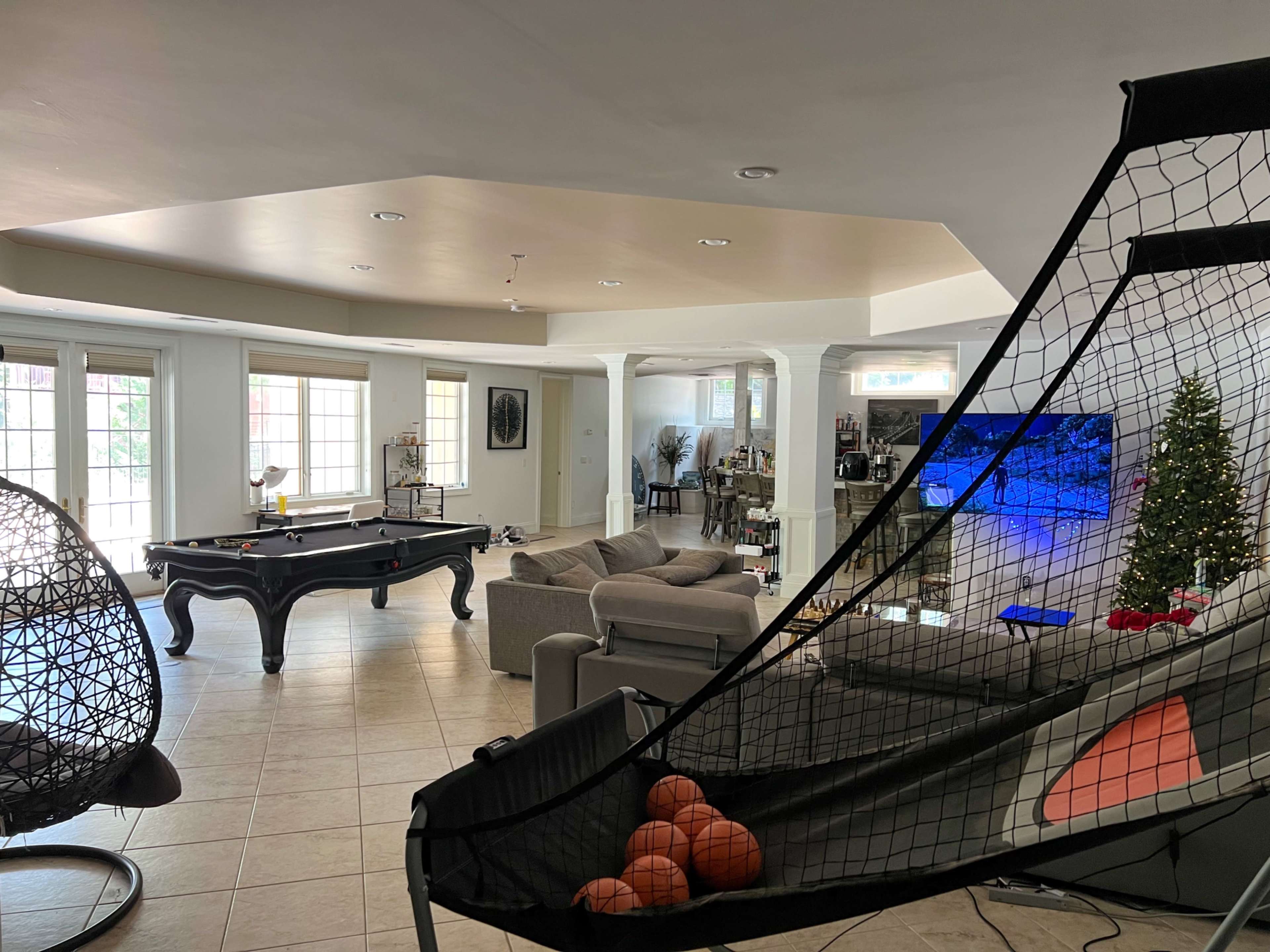 A spacious living room featuring a pool table, a large television, a basketball shooting arcade game, and a Christmas tree in the corner.