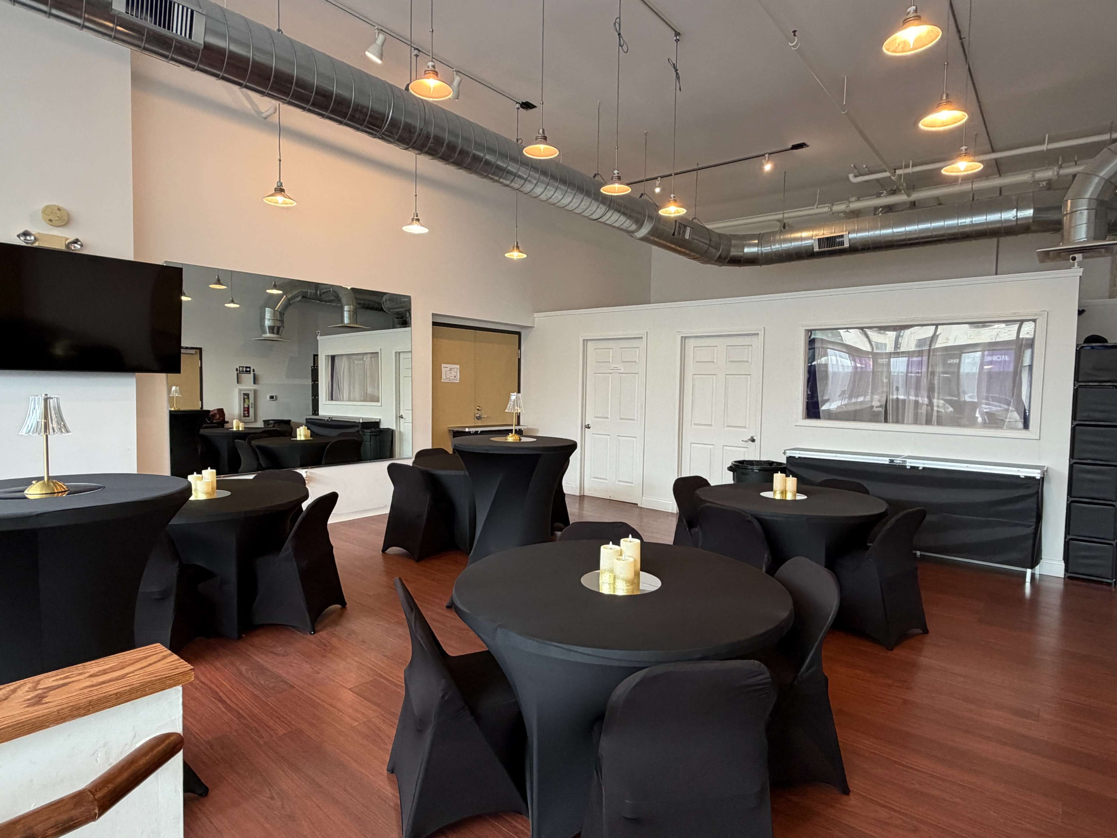 The image shows a well-lit event space featuring black tables and chairs, with decorative candles on each table and a large mirror on one wall.
