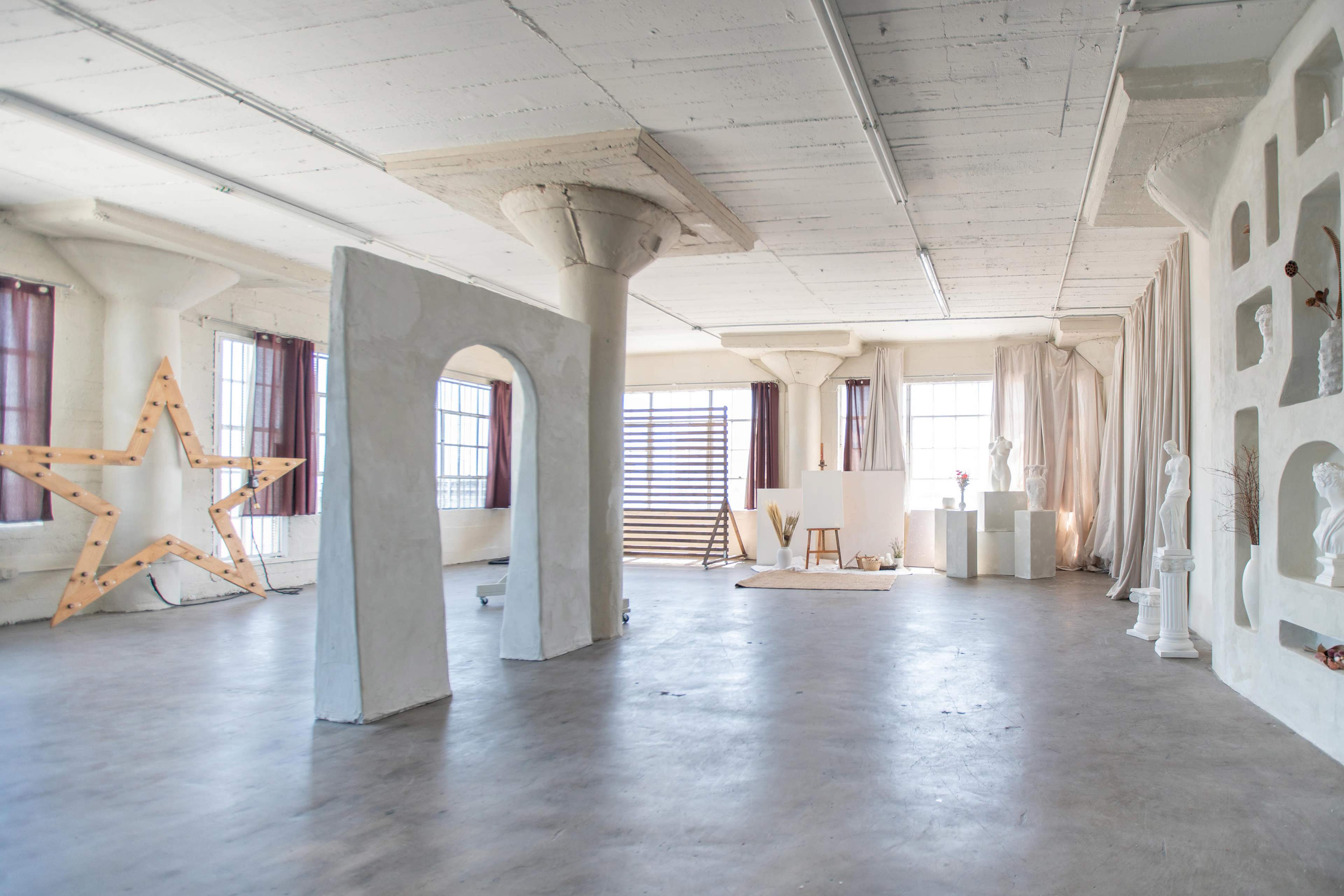 The image shows a spacious, well-lit interior with sculptural elements, large windows, and minimalist decor, featuring a prominent wooden star and various artistic installations.