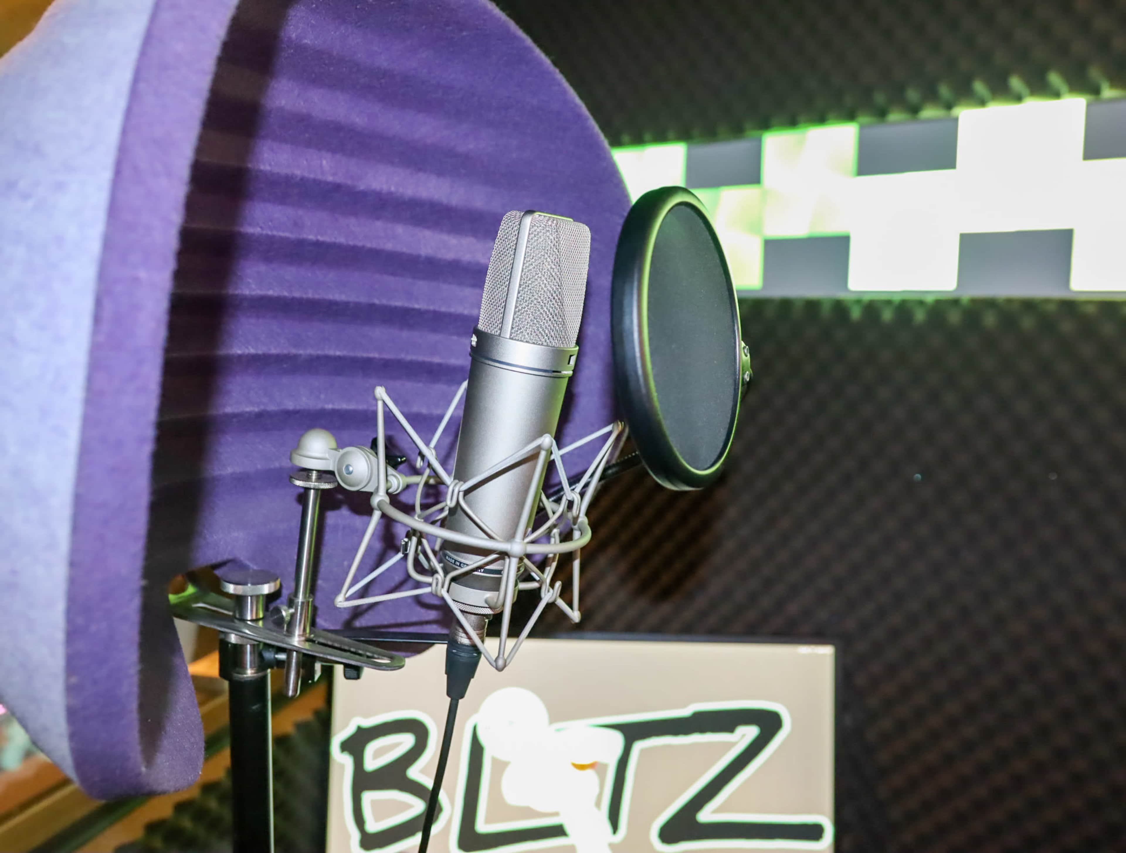 A microphone is set up in a soundproof recording environment with a purple pop filter in the foreground.