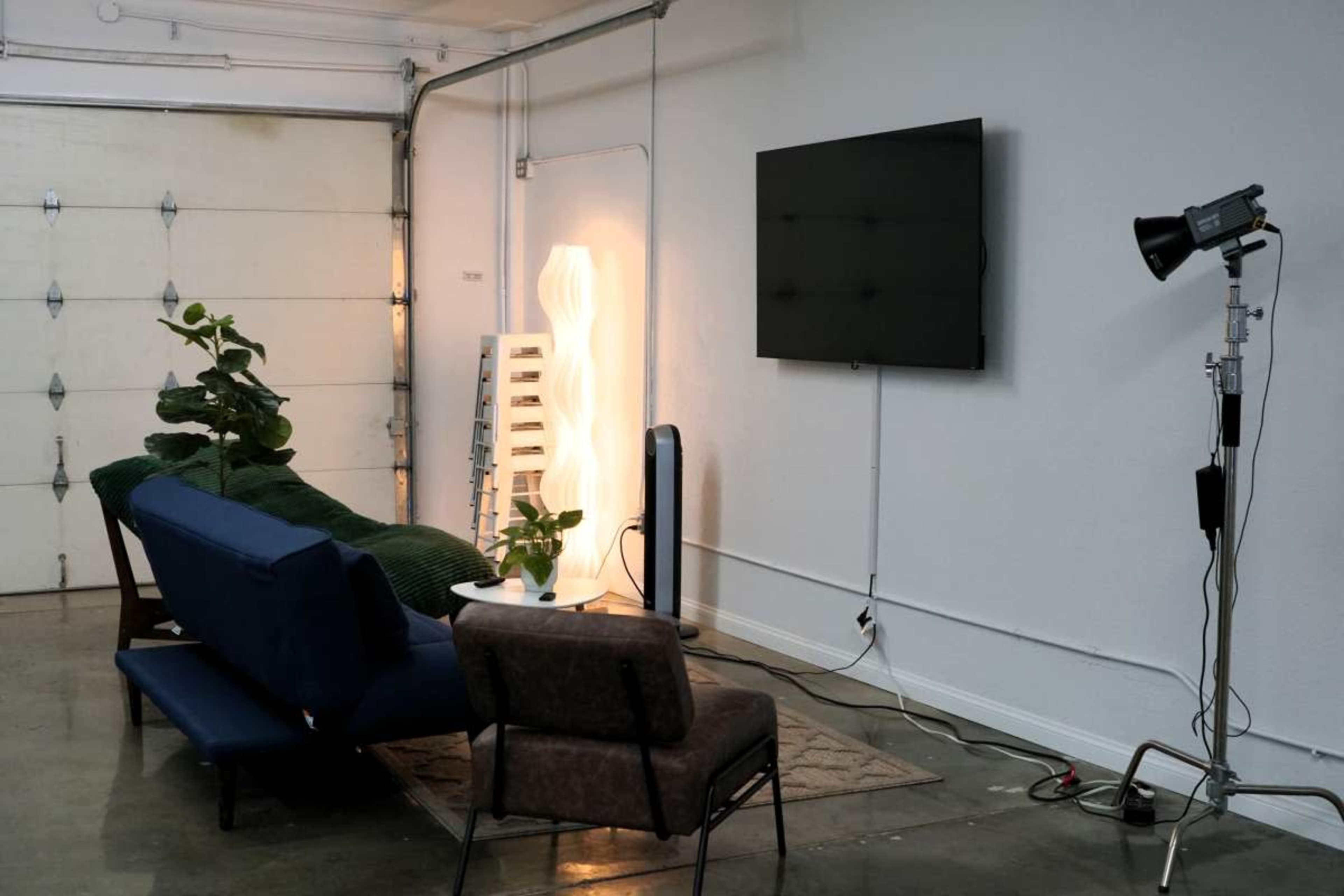 The image shows a modern living space in a garage, featuring a sofa set, a floor lamp, a TV mounted on the wall, and various decorative elements.