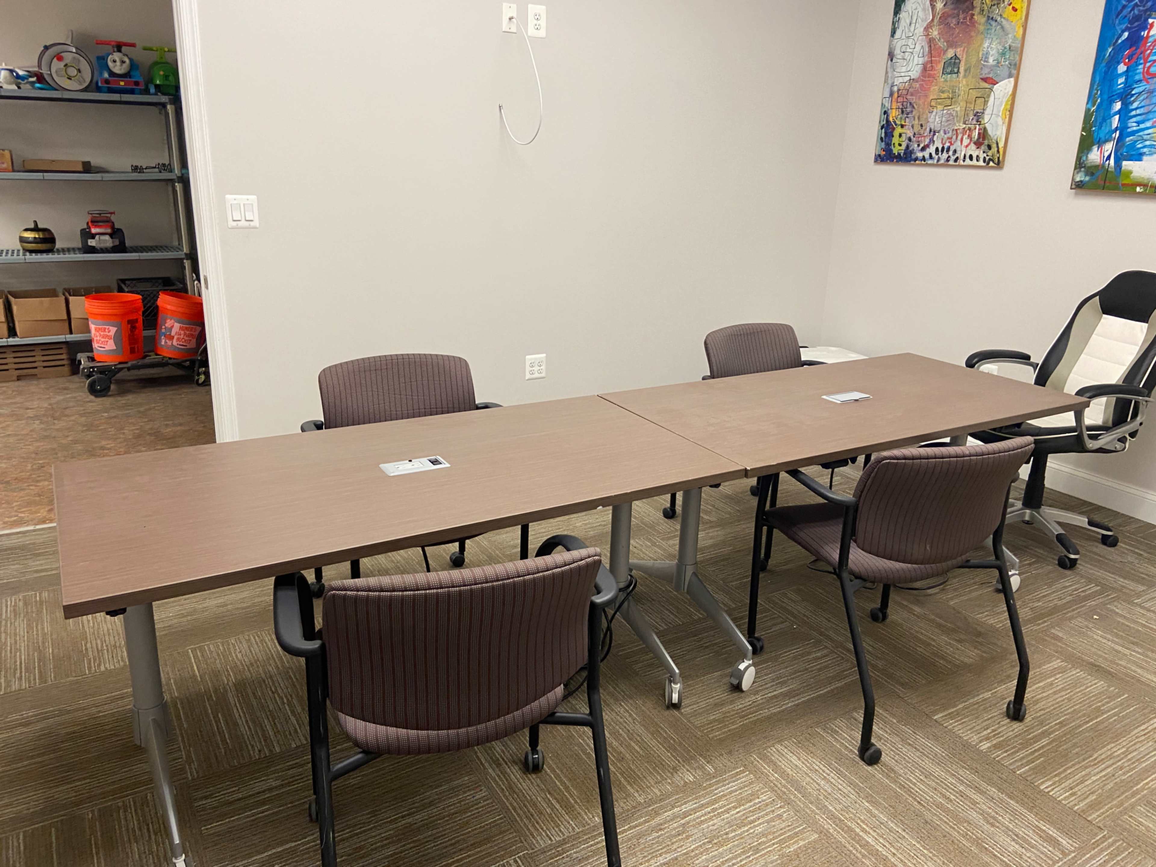 A meeting room features a long table set for four chairs, with office supplies placed at each seat.