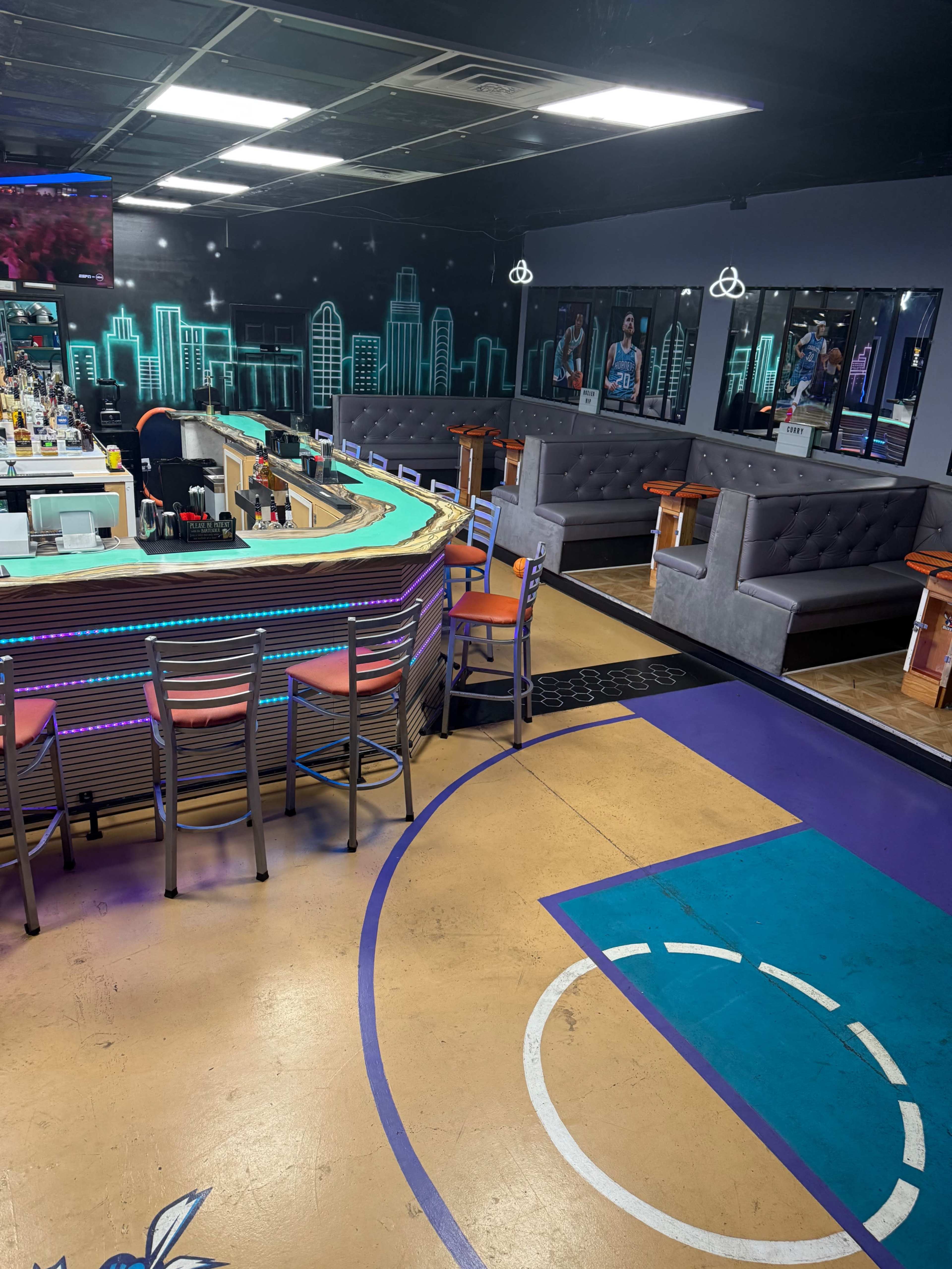 The image shows a sports-themed bar with colorful seating, a curved bar area, and a basketball court design on the floor.