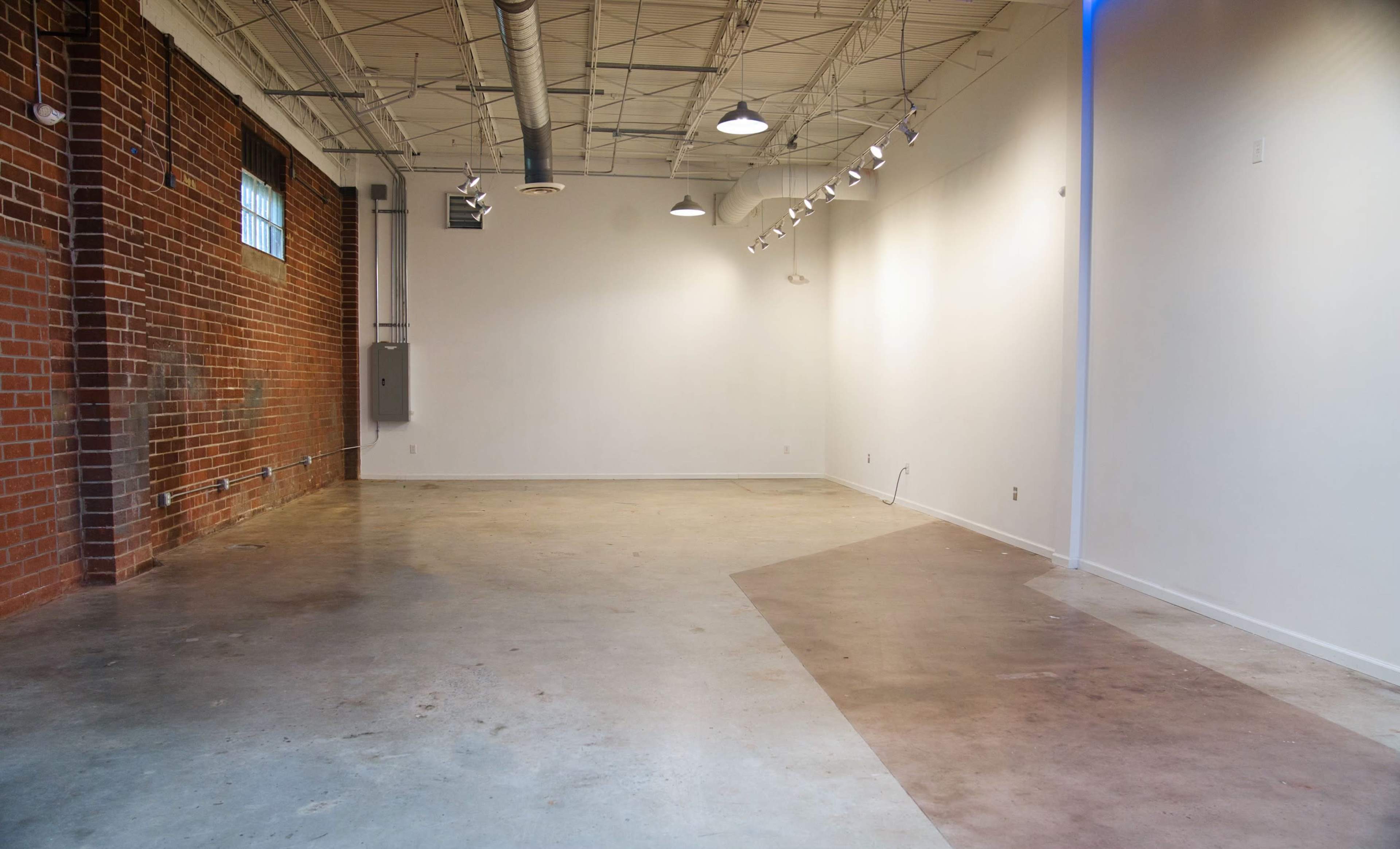 An empty, well-lit room with a polished concrete floor and exposed brick walls.