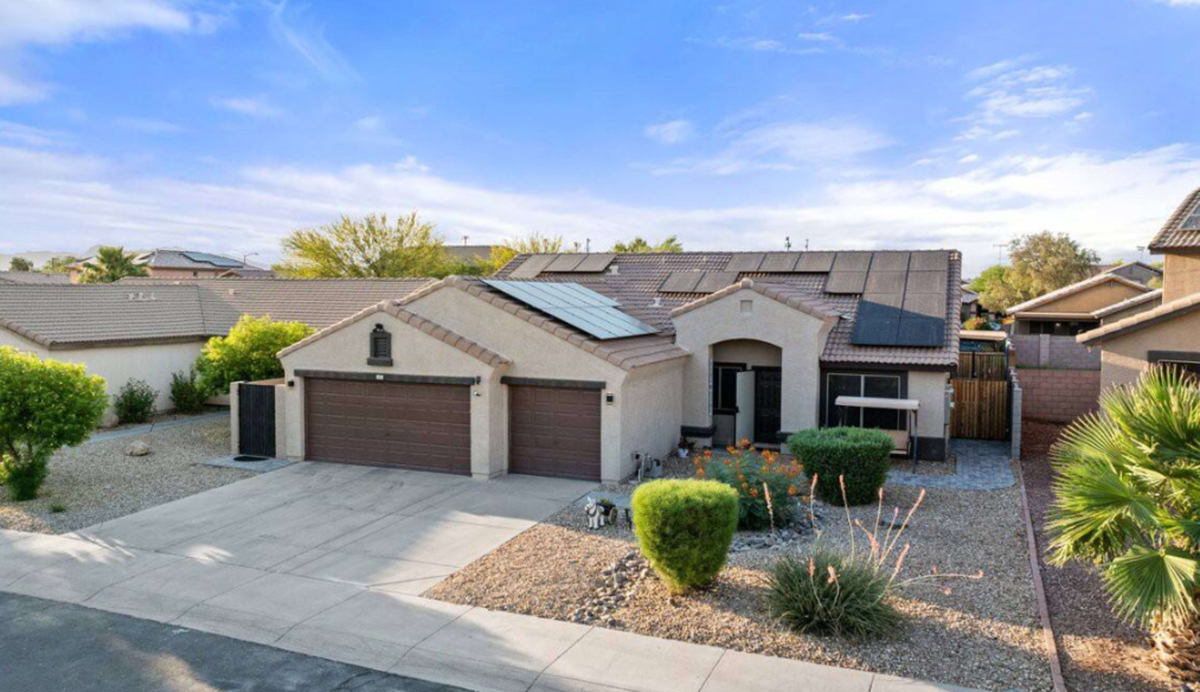 A single-story home with solar panels on the roof and a landscaped front yard is situated on a residential street.