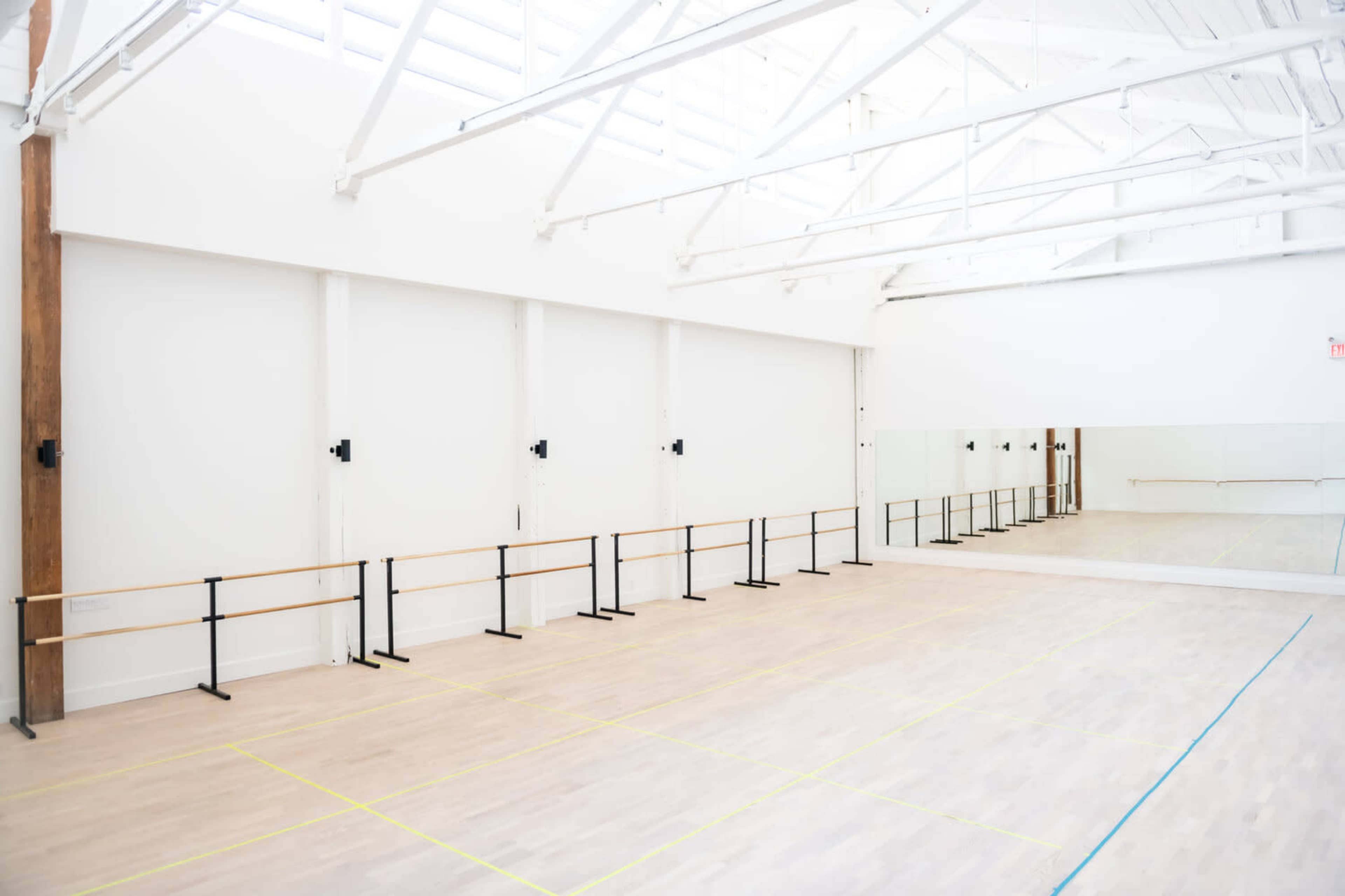 A spacious dance studio features wooden ballet bars lining the walls and mirrors reflecting the open area.