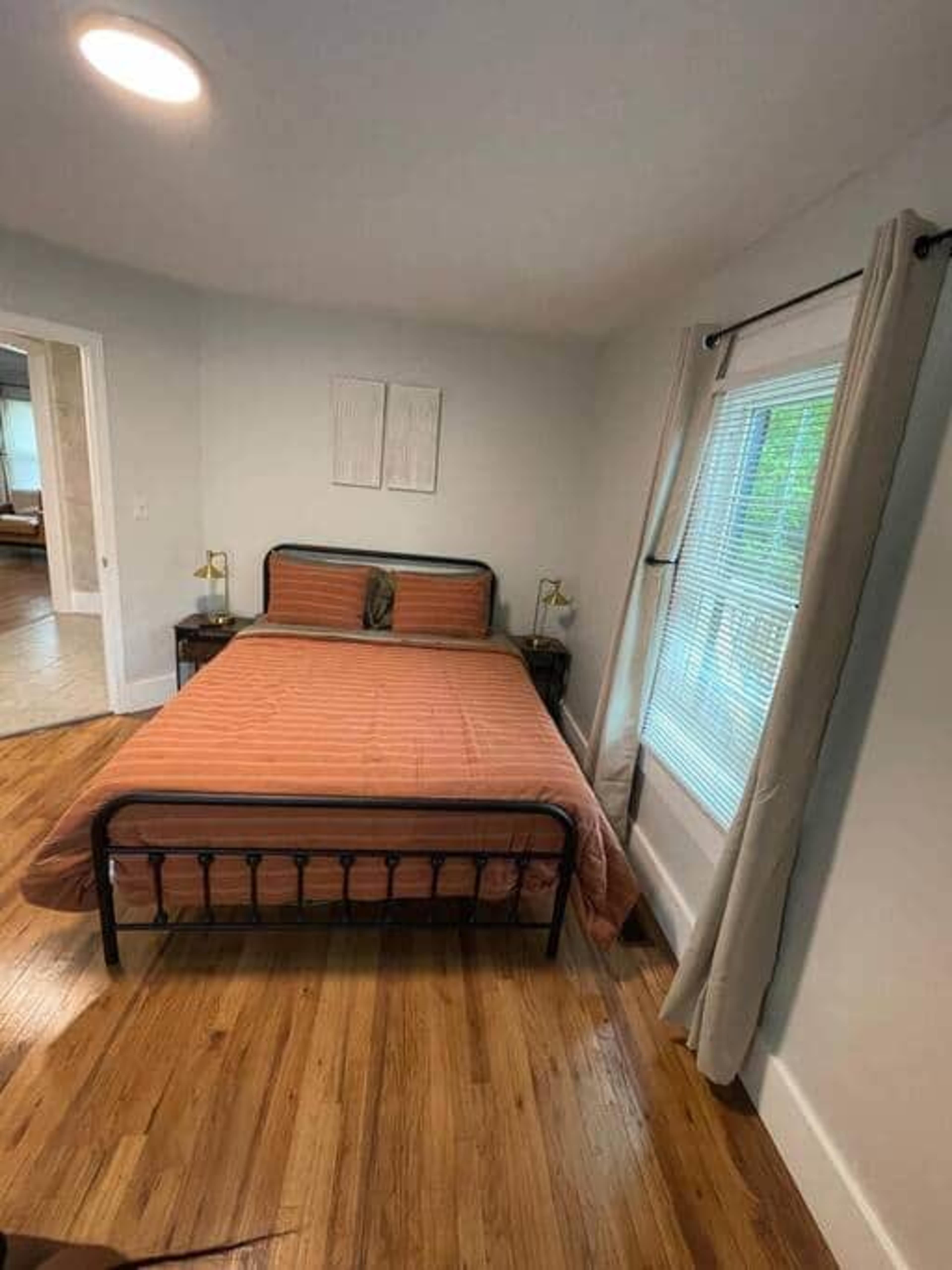 A neatly arranged bedroom with a metal-framed bed, orange bedding, and light-colored walls.