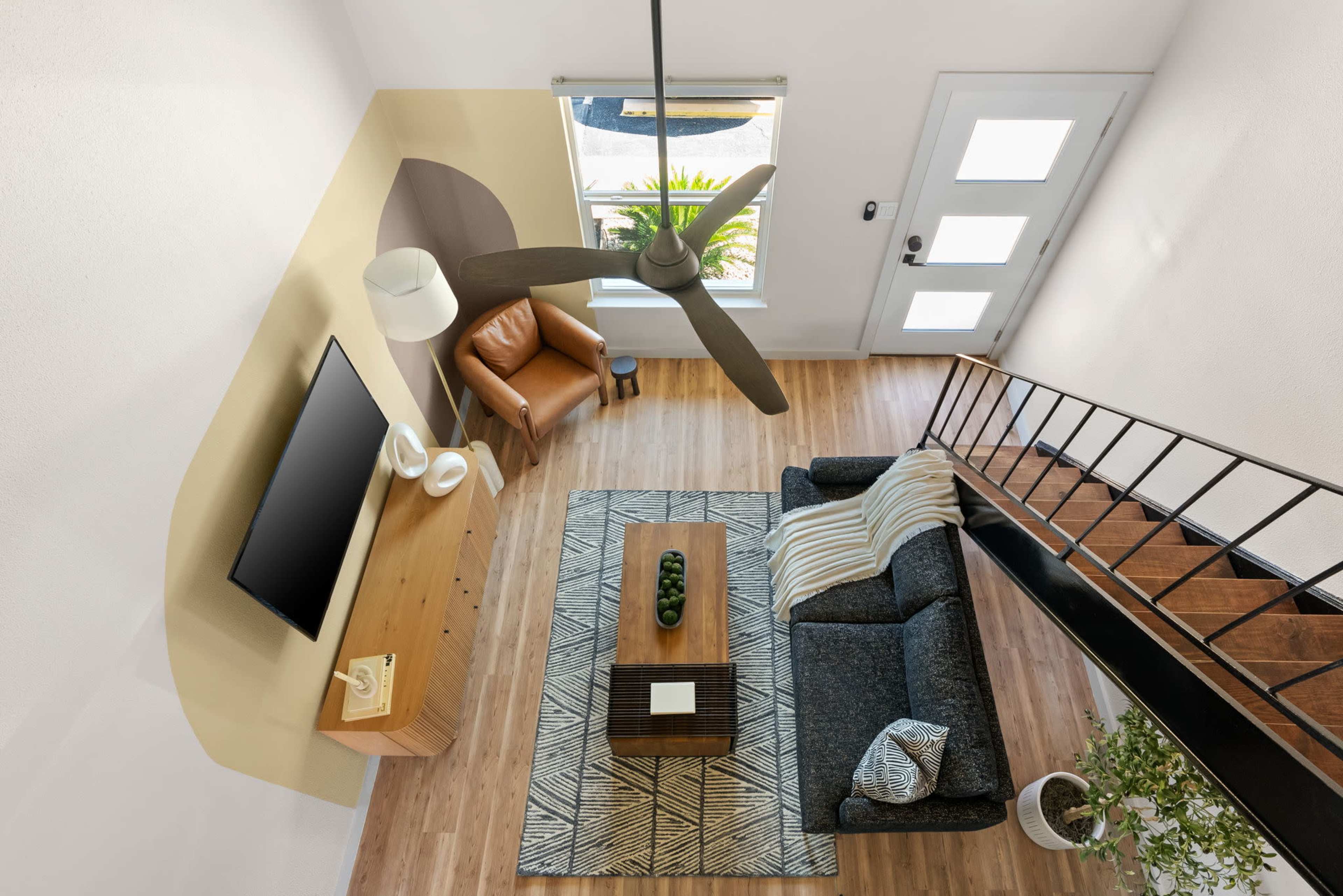 The image shows a modern living room with a gray sofa, wooden coffee table, and a television mounted on a wall, all viewed from an overhead angle.