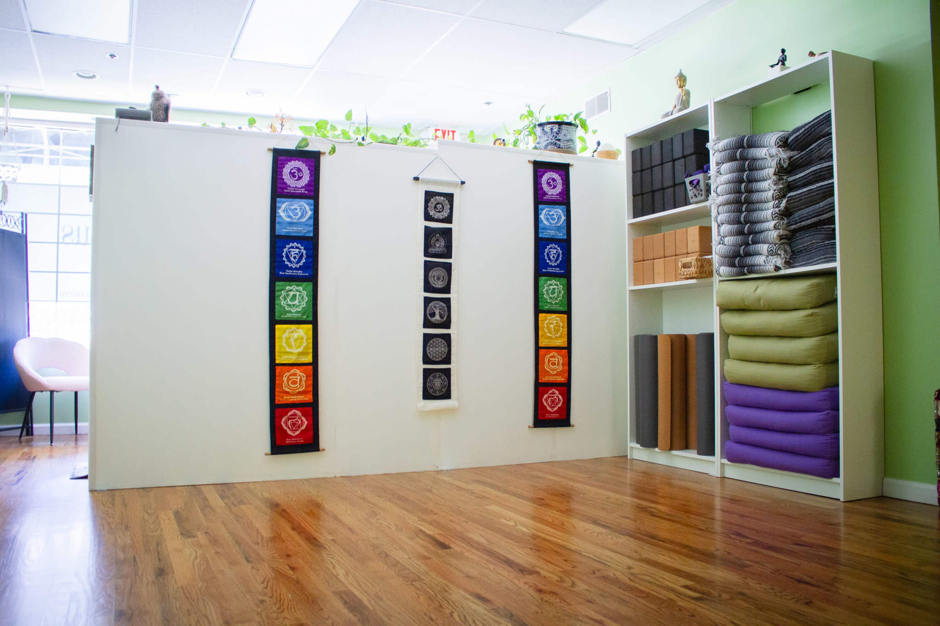The image shows a yoga studio interior with a wall adorned with chakra banners and shelves stocked with yoga mats and blankets.
